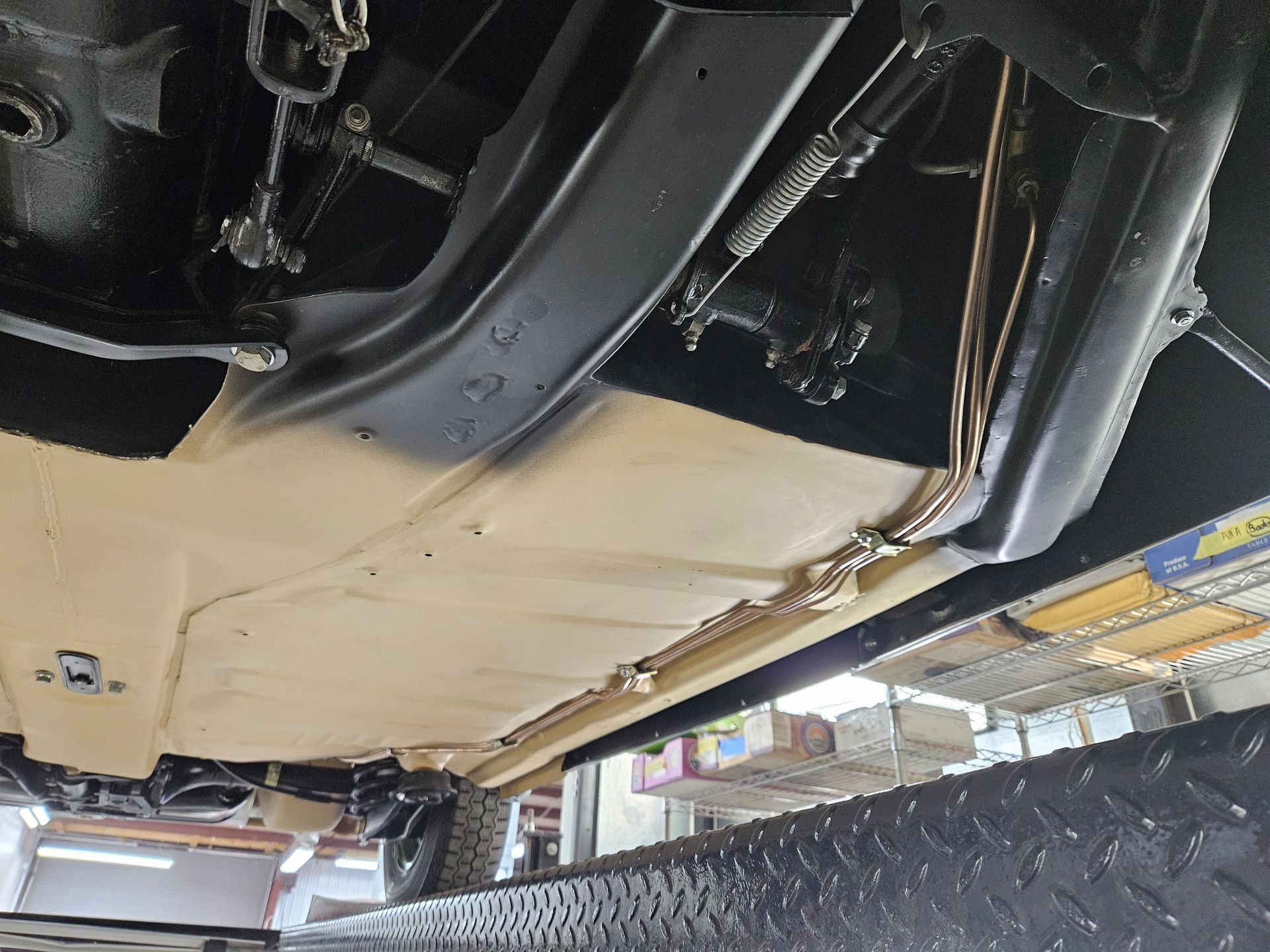 Underside of a vehicle painted tan and black on a lift, showing chassis and components.