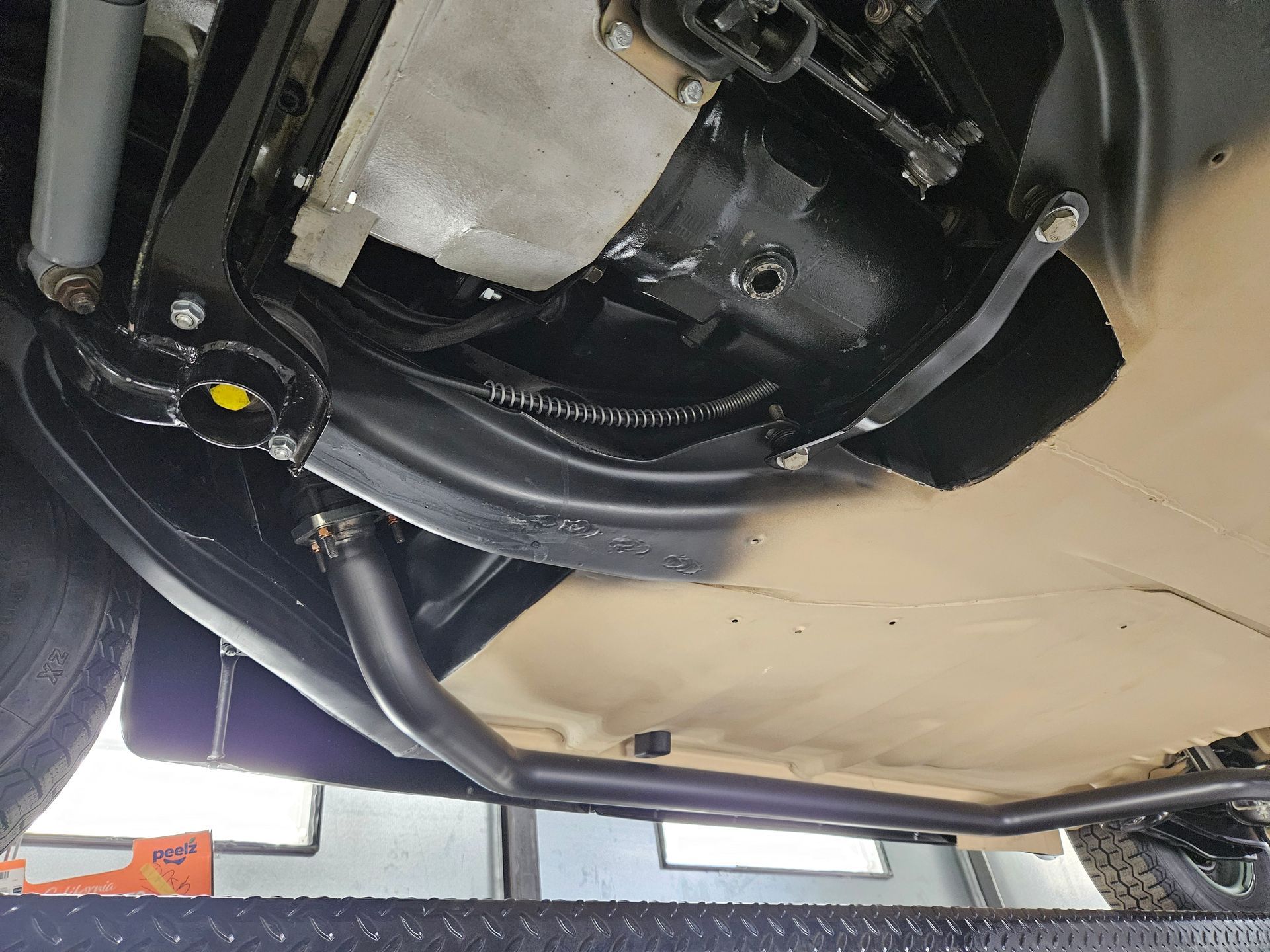 Undercarriage view of a vehicle on a lift, showing black exhaust pipe, suspension, and mechanical components.