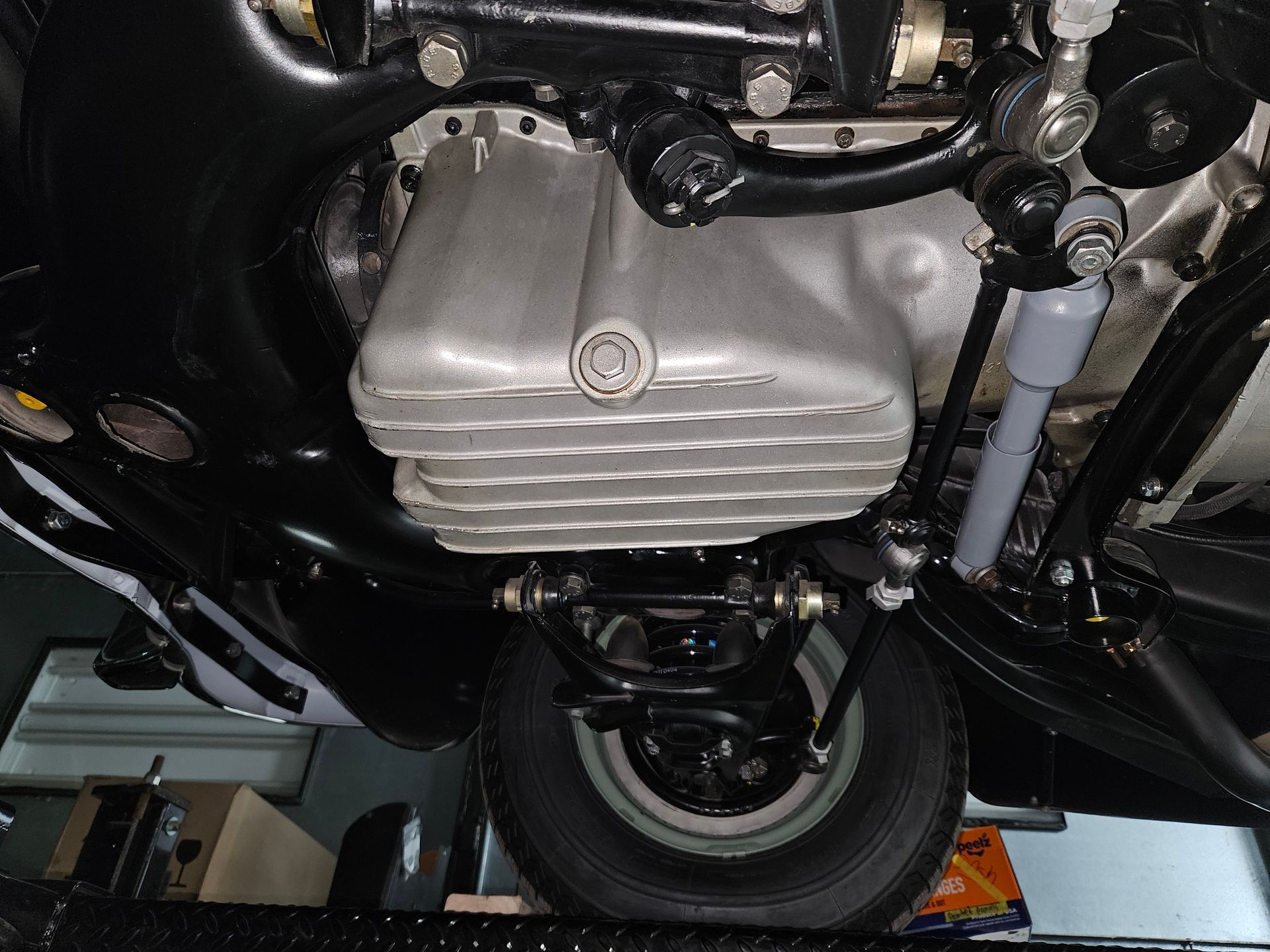 Underside view of a vintage car chassis; oil pan is center, suspension and tire visible.