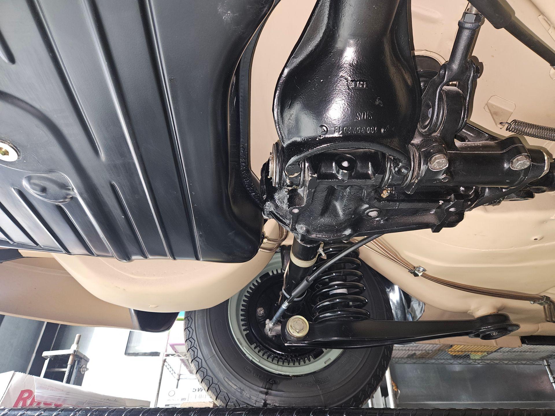 Undercarriage of a black painted vintage vehicle, showing suspension components and a rear wheel.