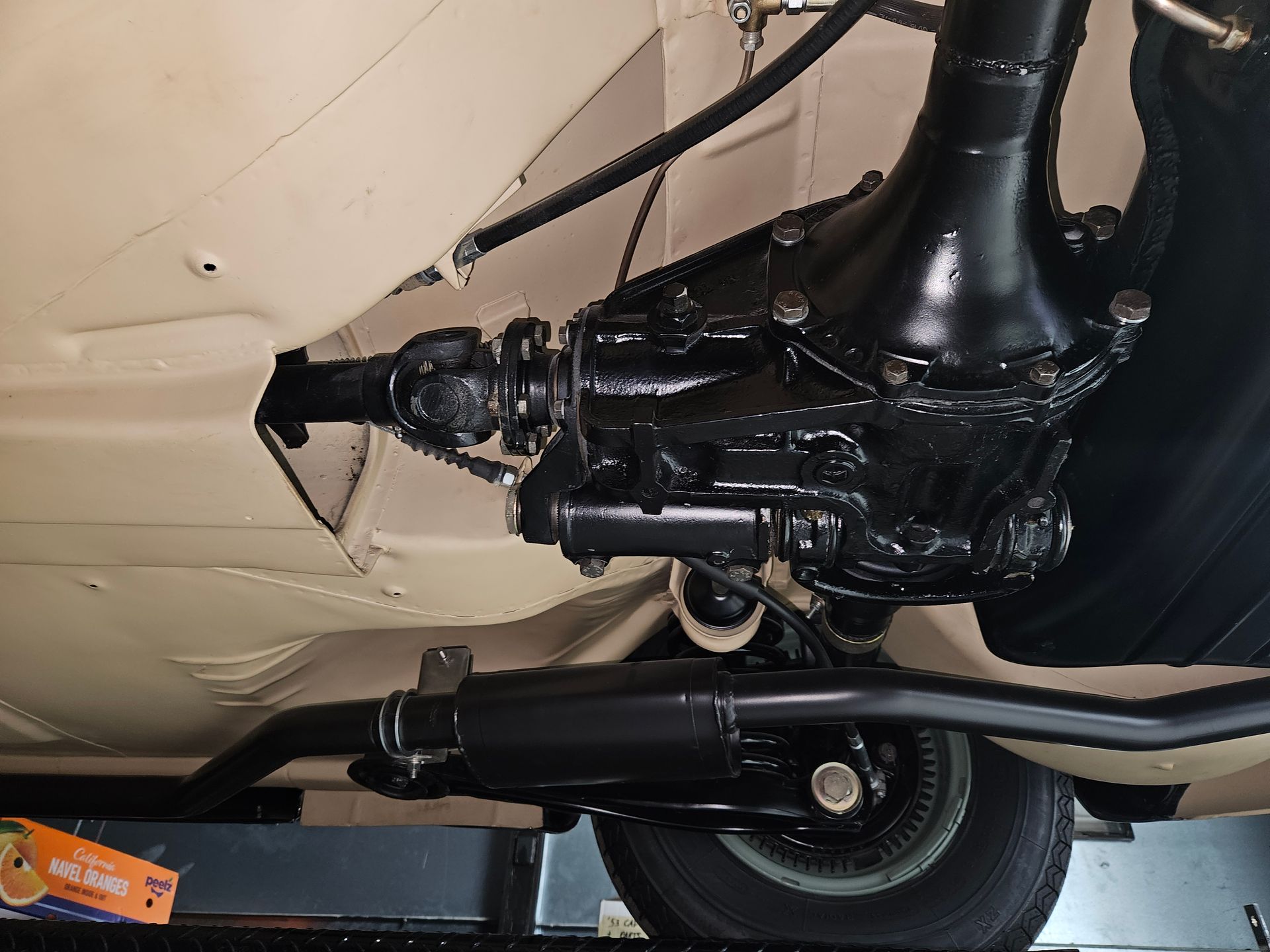 Underside of a car showing a black differential, driveshaft, and exhaust system. Beige car body, black components.