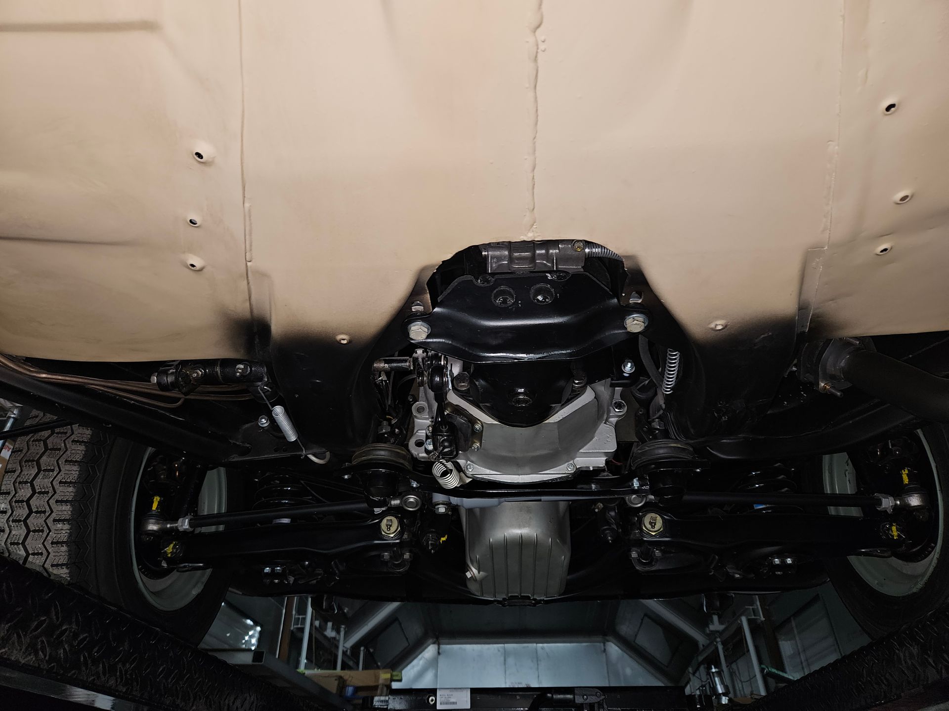 Undercarriage of a black and tan vehicle on a lift. Shows the engine and suspension components.