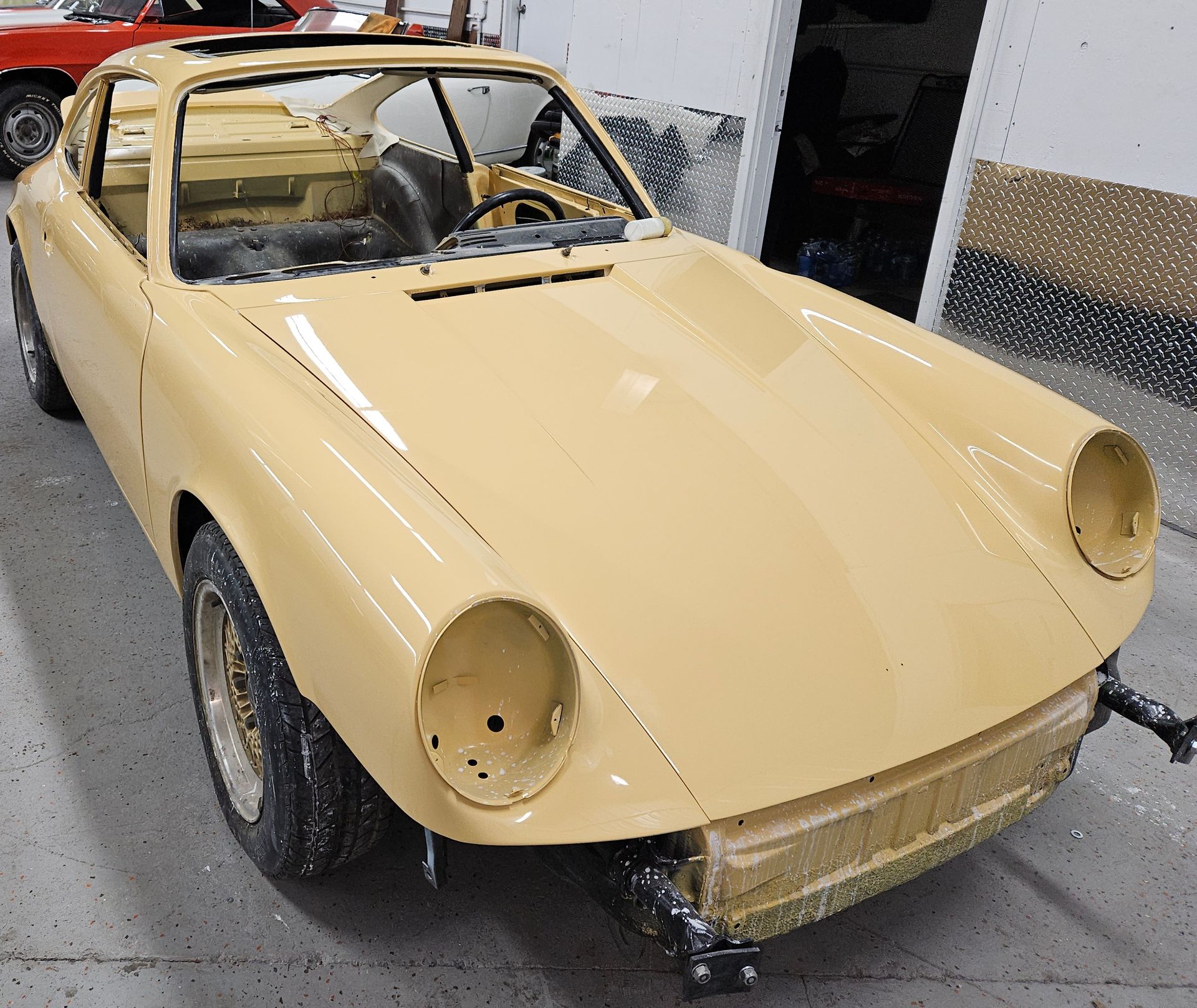 Yellow classic sports car in a garage, missing parts.