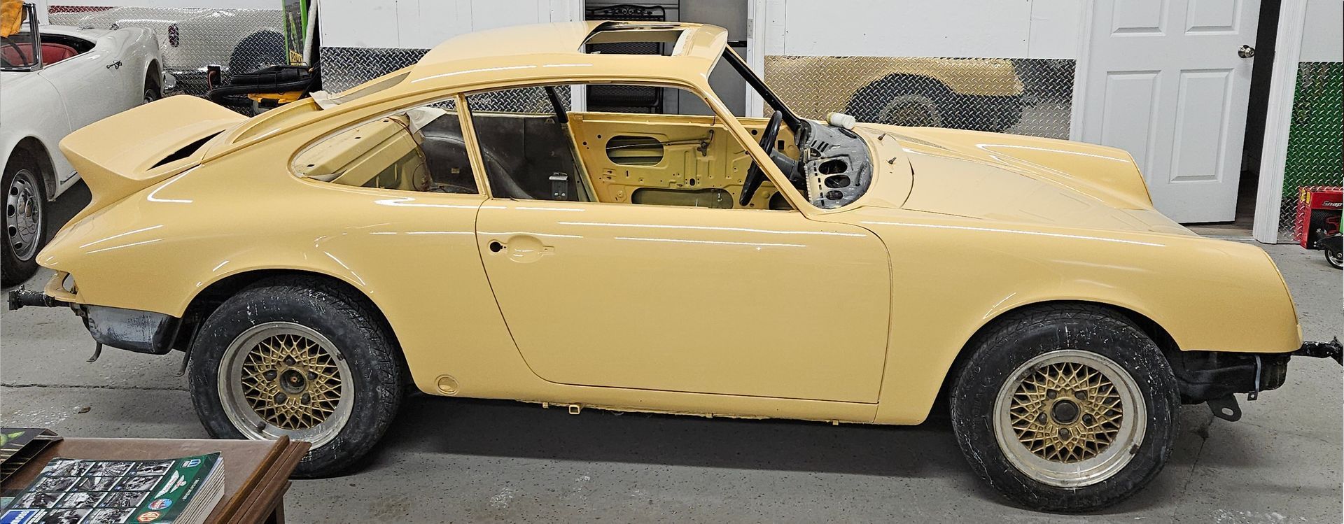 Yellow vintage Porsche 911 undergoing restoration in a workshop.