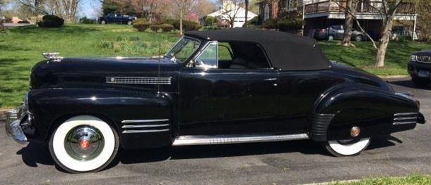 Black vintage convertible car with white wall tires parked on a driveway.