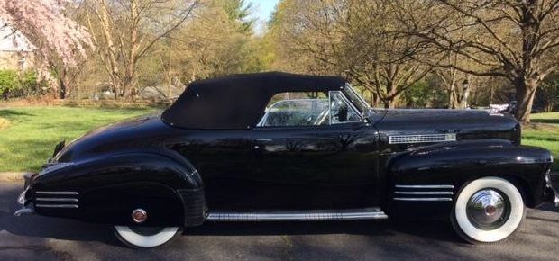 Black vintage convertible car with white wall tires parked on a road.
