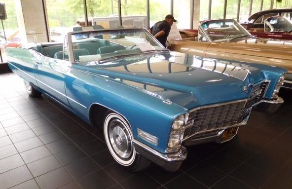 Blue convertible Cadillac on display in a showroom, white wall tires, chrome grille.