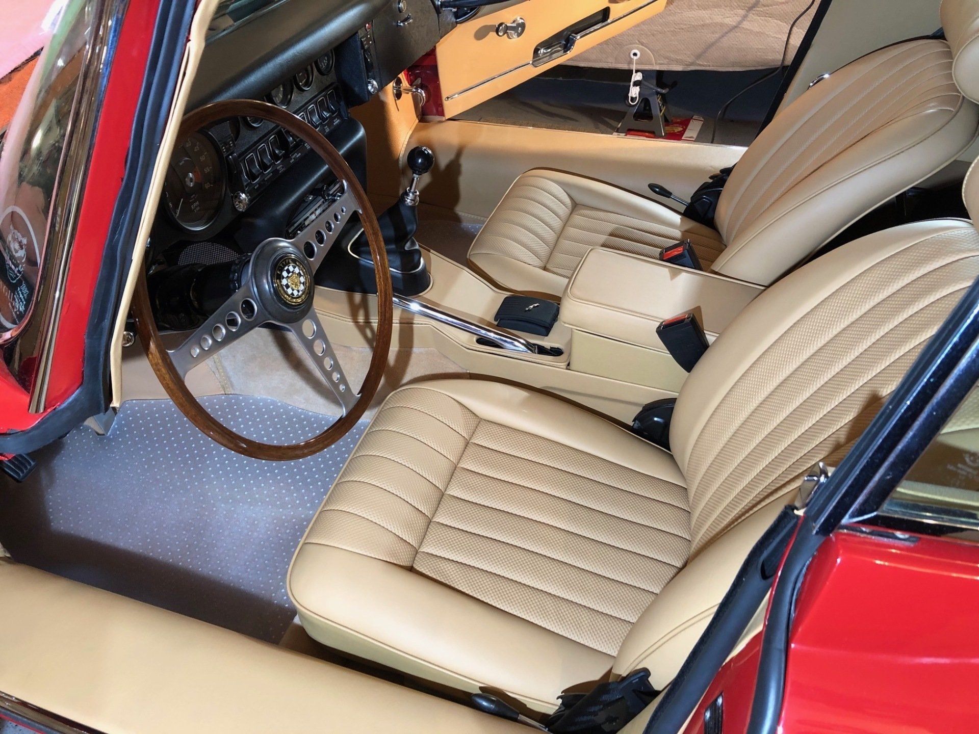 Interior of a classic red Jaguar with tan leather seats and a wooden steering wheel.