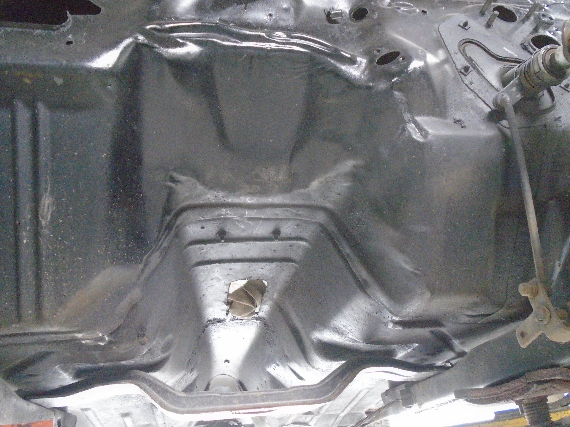 Underside of a car's black chassis, showcasing its structural design and central hole.