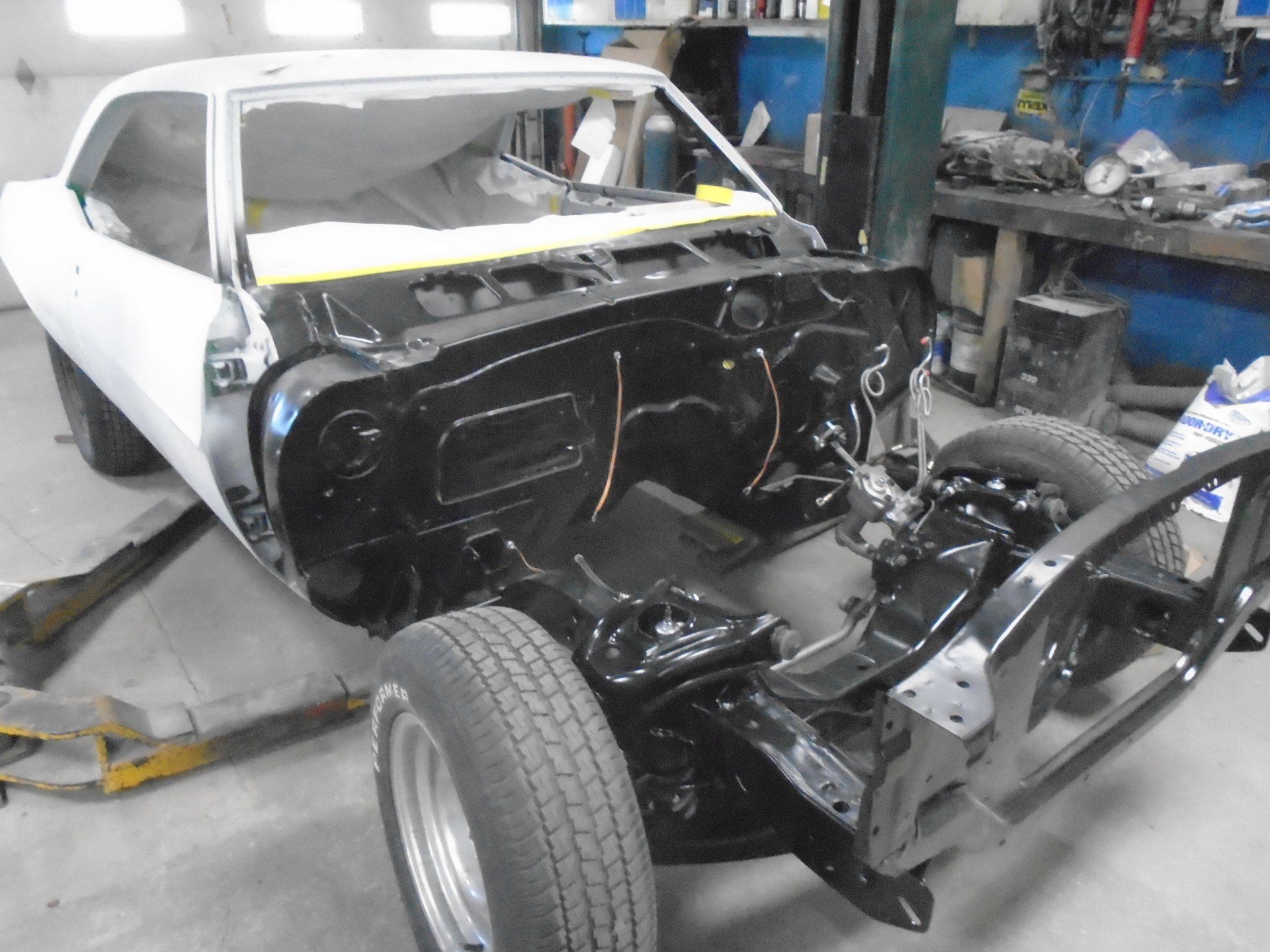 White classic car body, black chassis, in a workshop, under restoration.