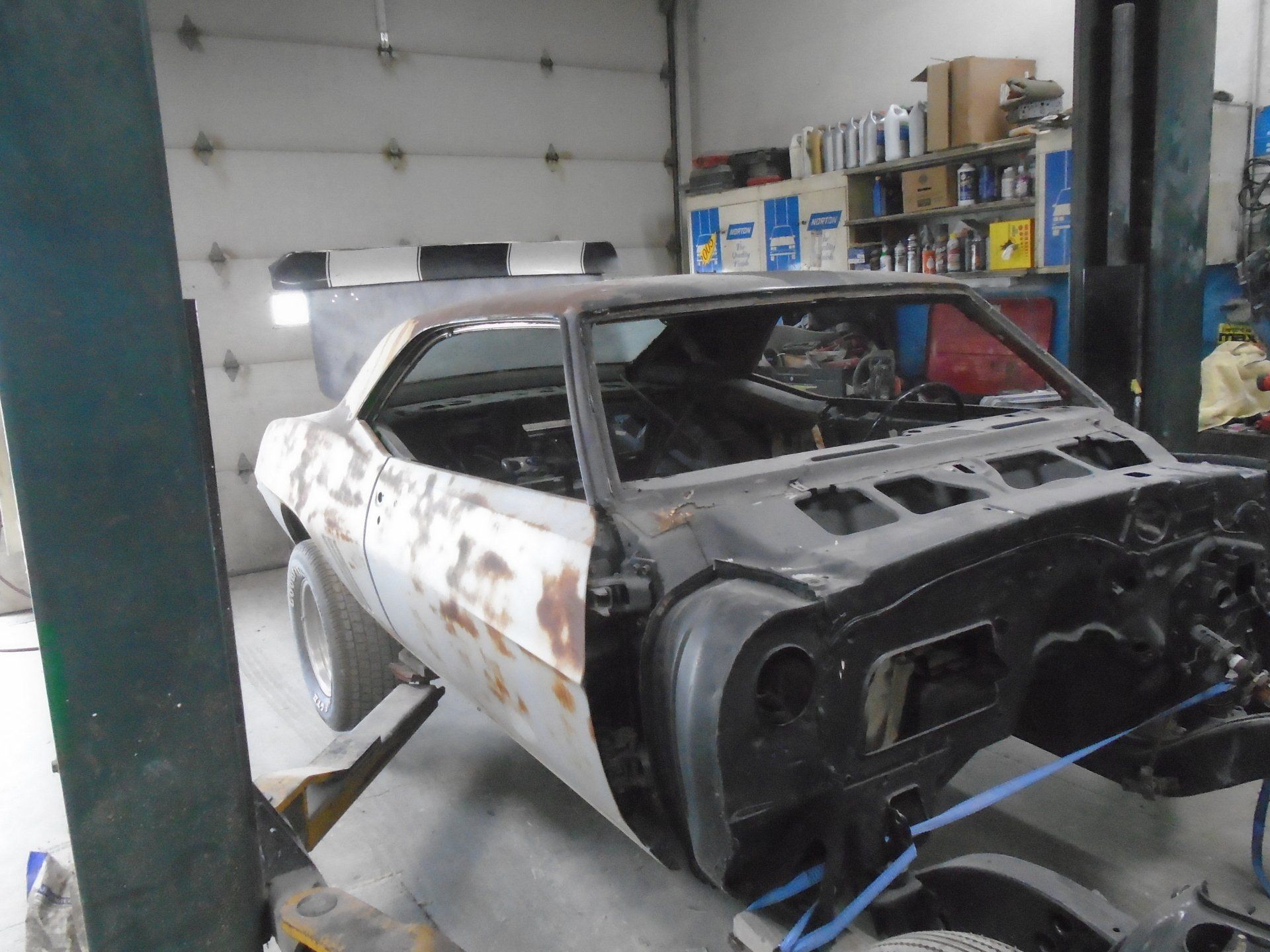 Partially disassembled classic car in a workshop, raised on a lift. Rust and black paint visible.
