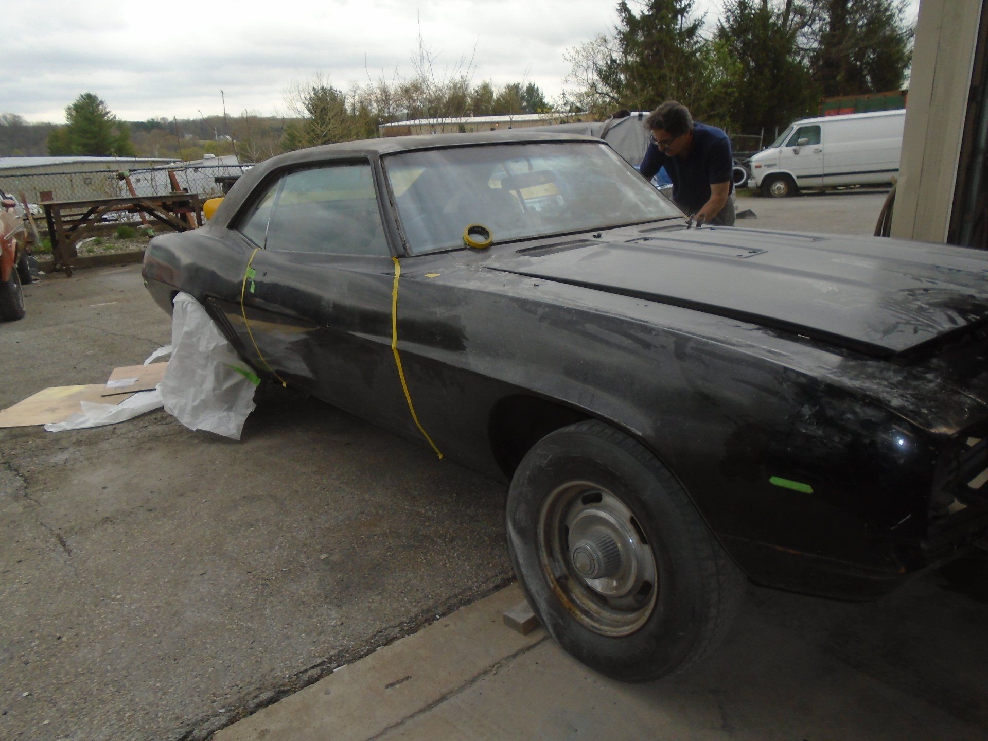 Black classic car being worked on in a garage; a person stands near the front.