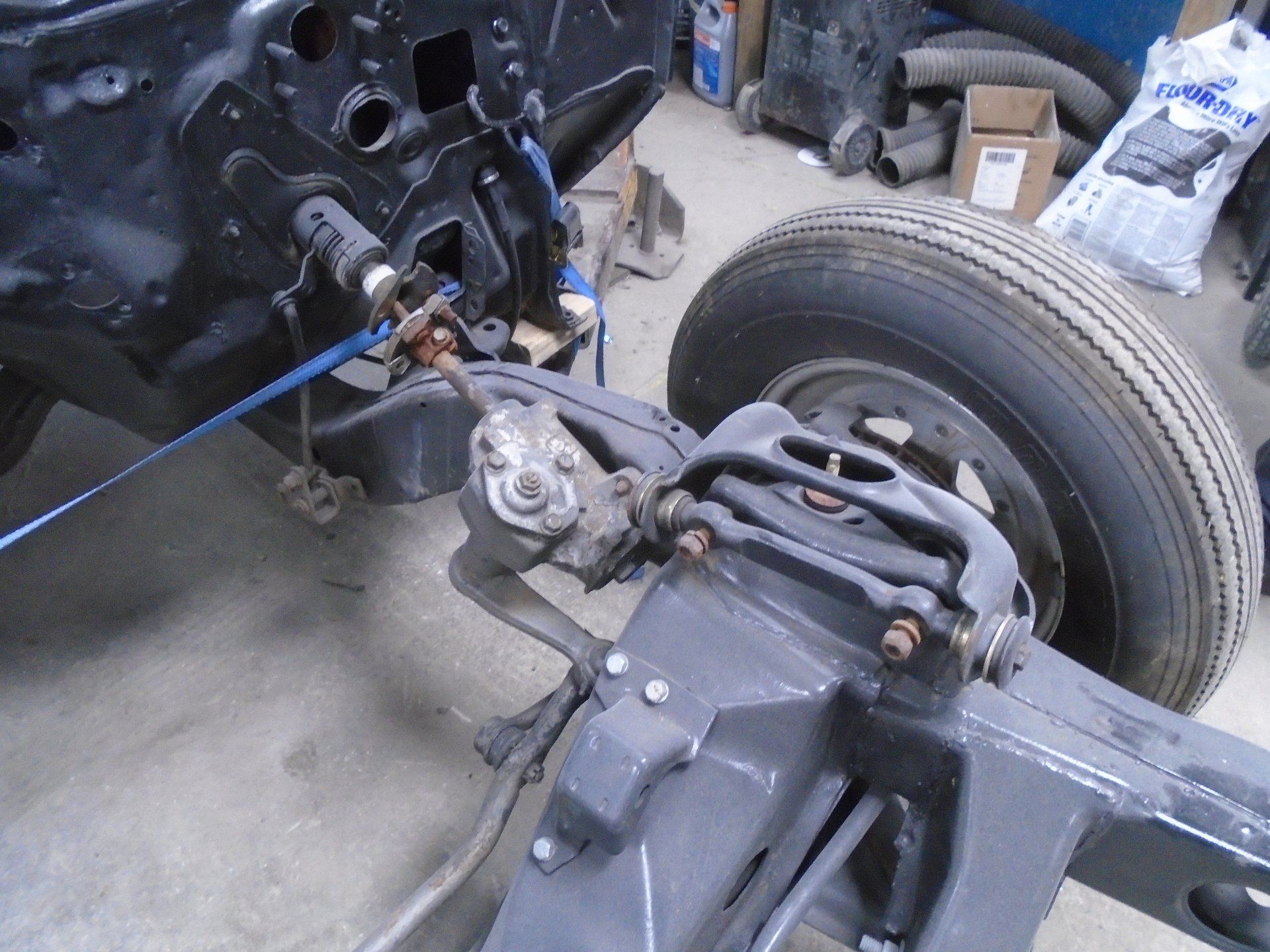 Black and gray car frame undergoing restoration, with steering components and tire visible.