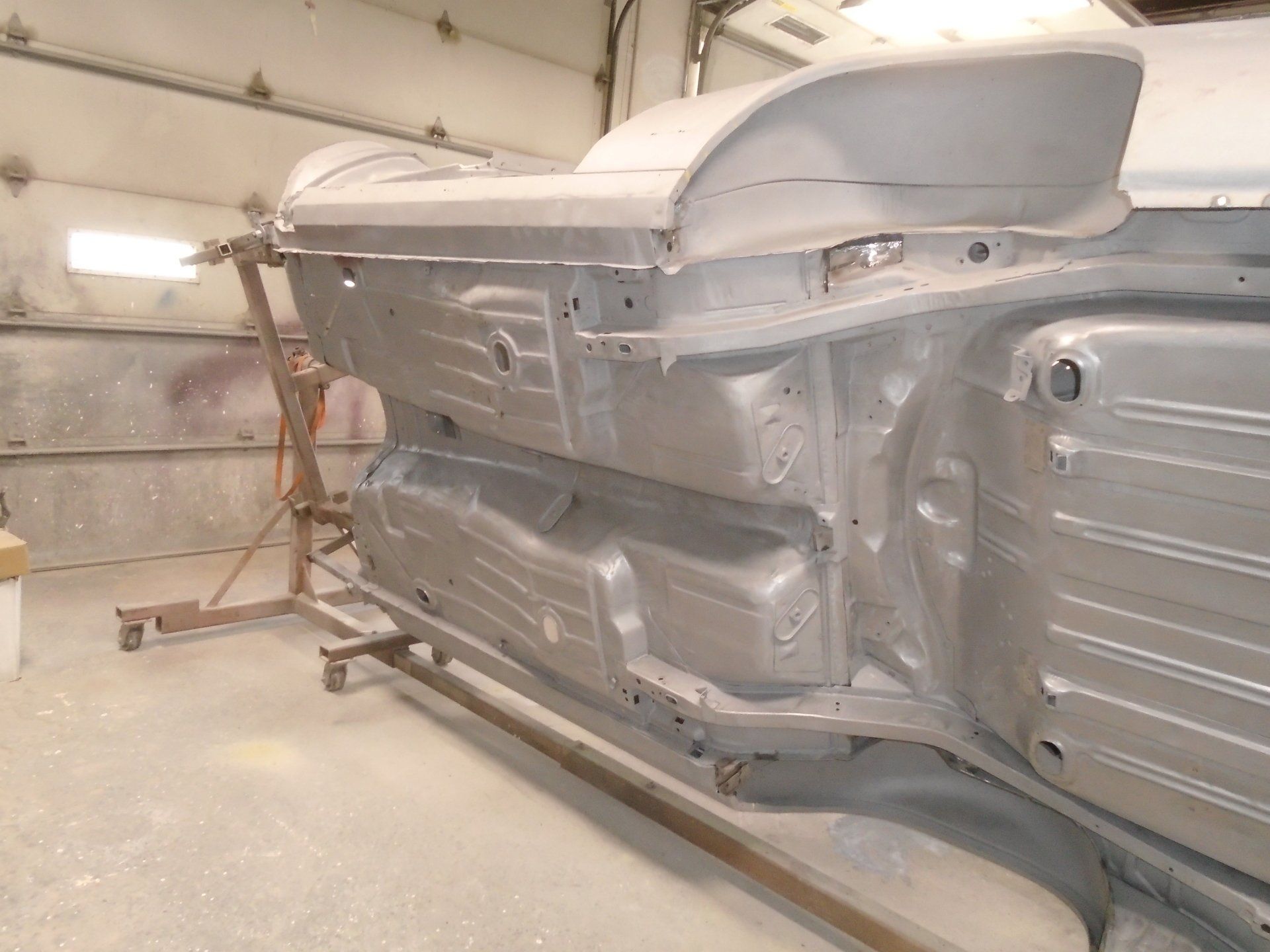 Underside of a car body being restored, painted silver, in a workshop.