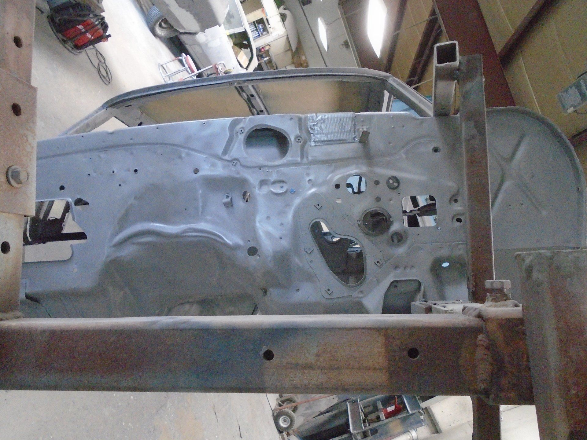 Bare car body frame inside a workshop, supported by metal beams.