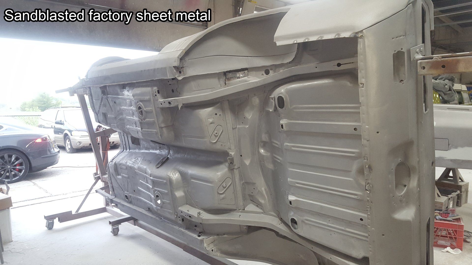 Sandblasted factory sheet metal underside of a vehicle, suspended in a workshop.