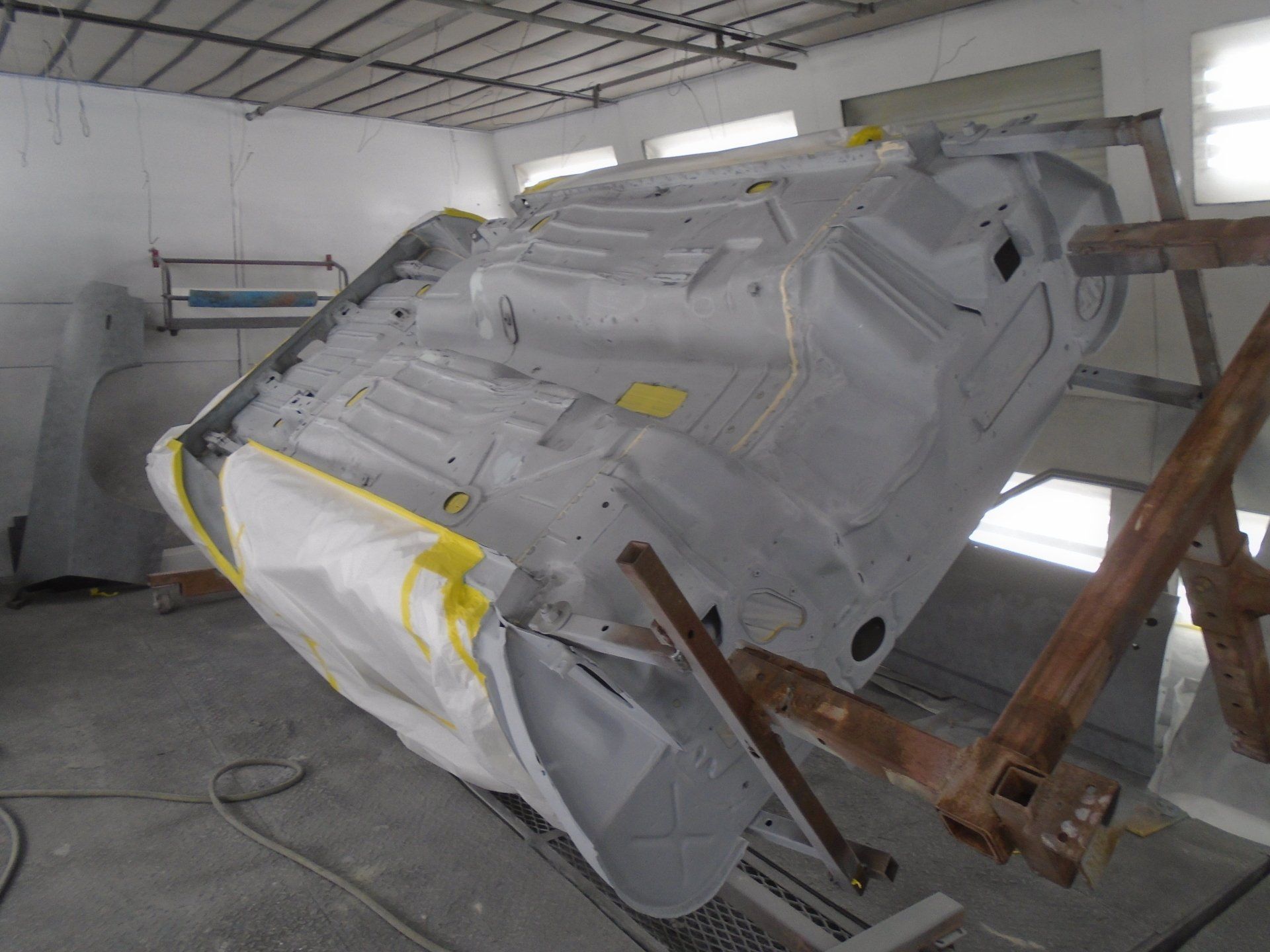 Underside of a light gray car body in a paint booth, taped for painting.