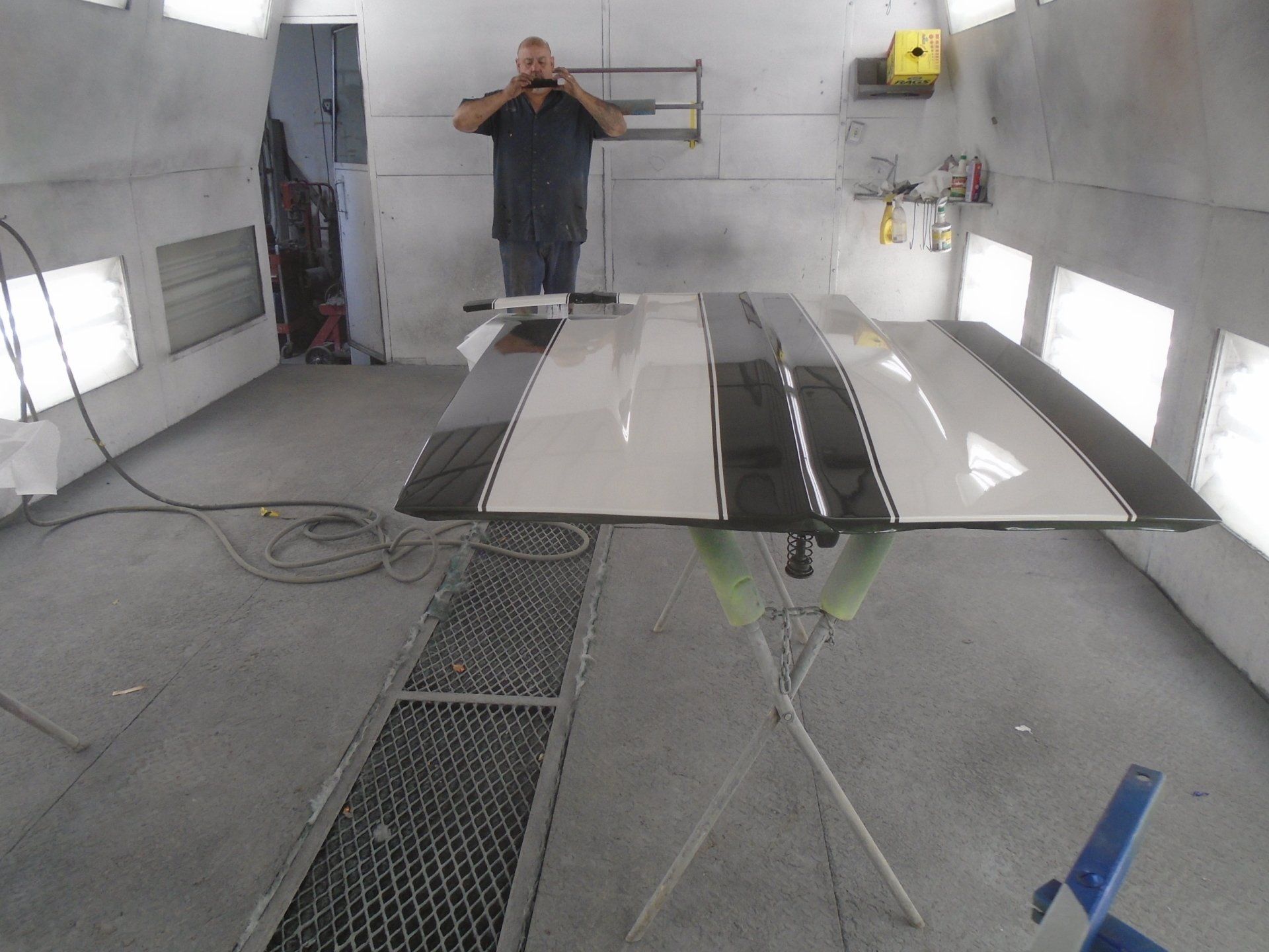 A person in a paint booth poses near a car hood with black and white stripes.