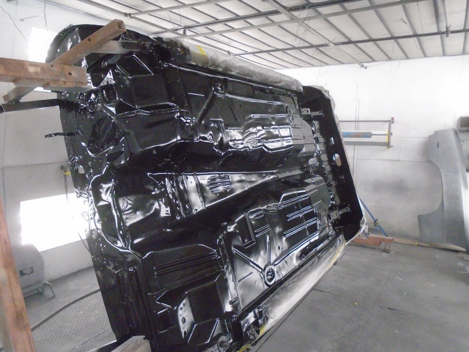 Underside of a car in a body shop, freshly painted black.