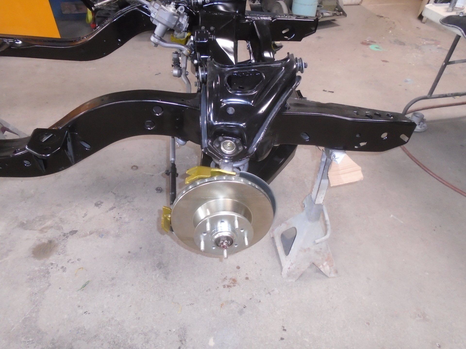 Black car chassis with new disc brake assembly installed, supported by a jack stand.