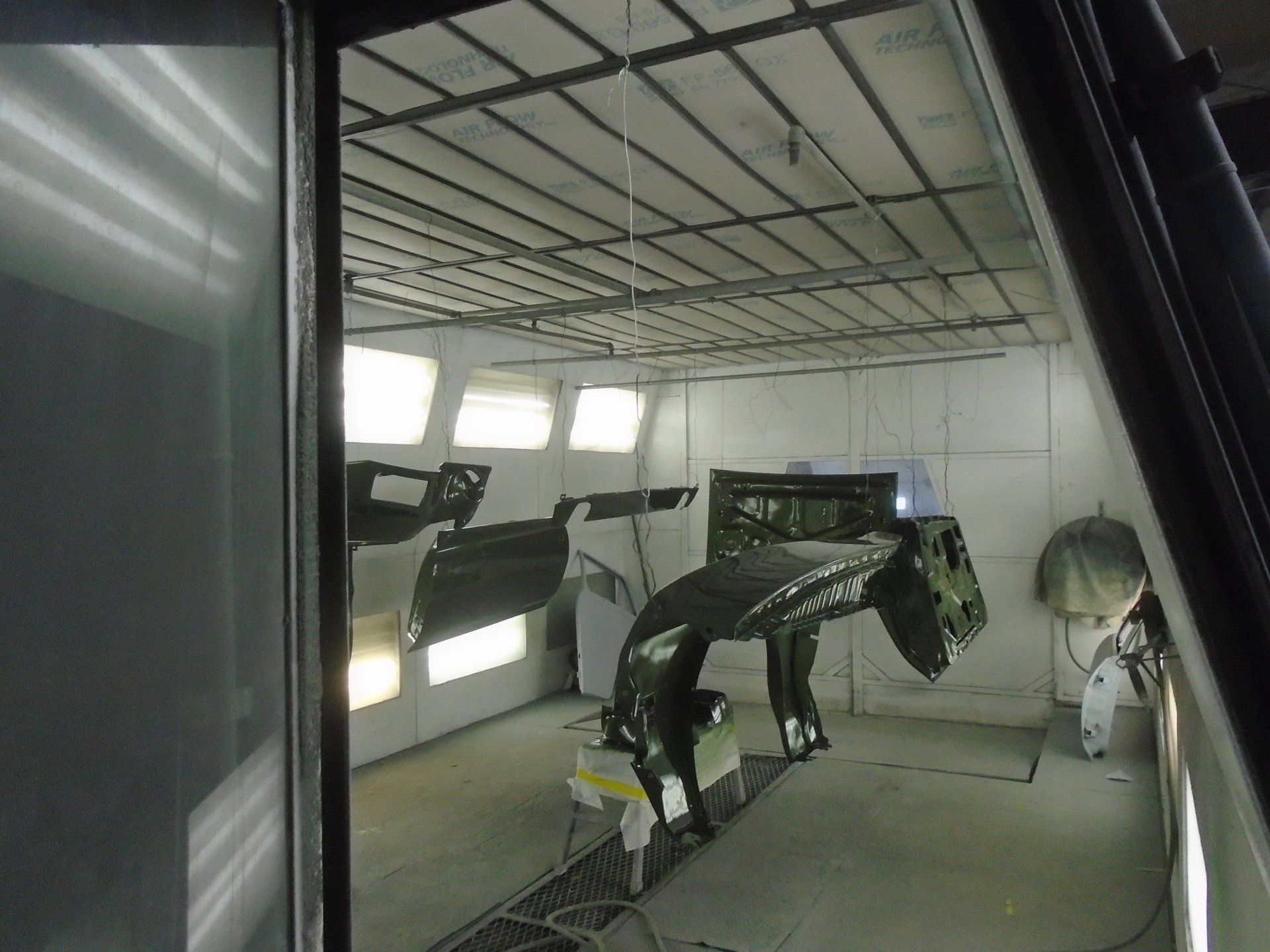 Car parts hanging in a paint booth, ready for painting. Interior setting, with green paint visible.