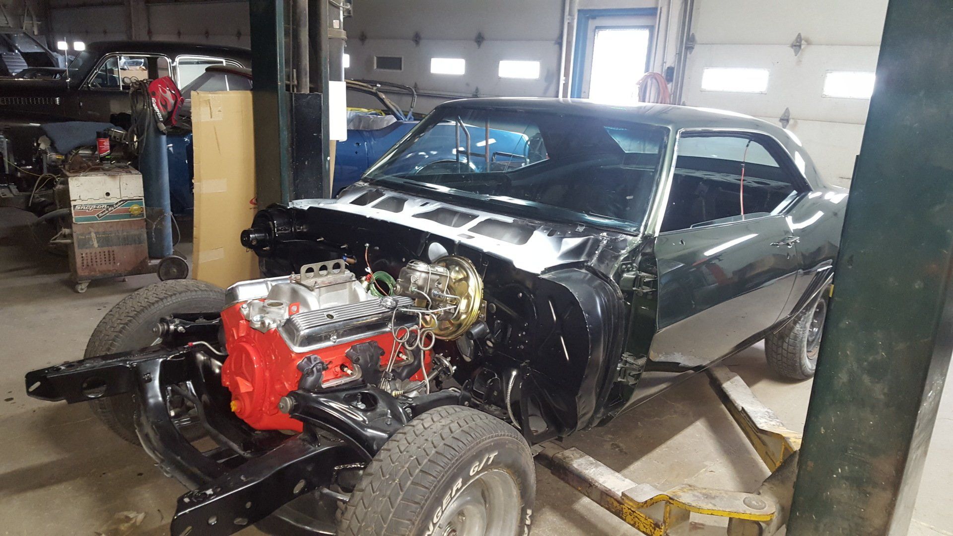 Dark green classic car in a shop, engine exposed, undergoing restoration.