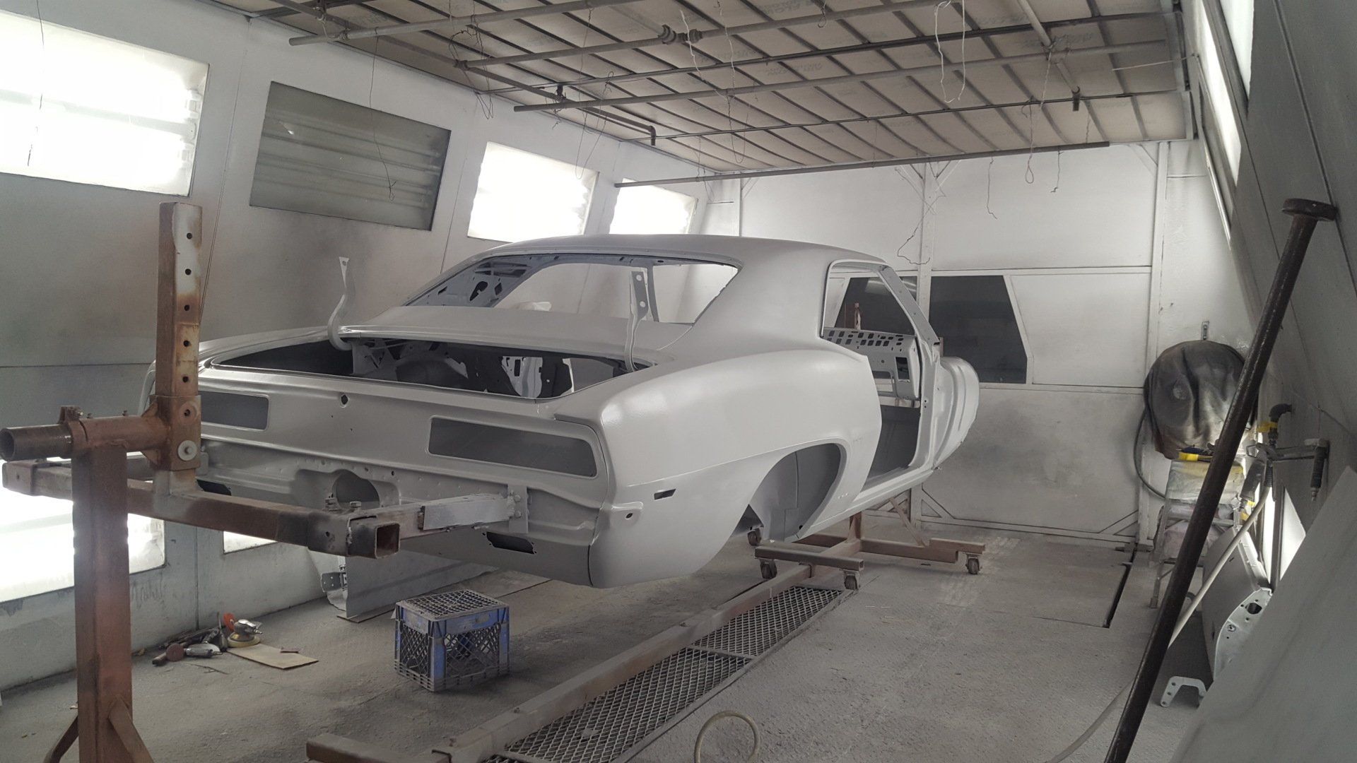 Classic car body in a spray booth, suspended on a rotisserie, prepped for painting.
