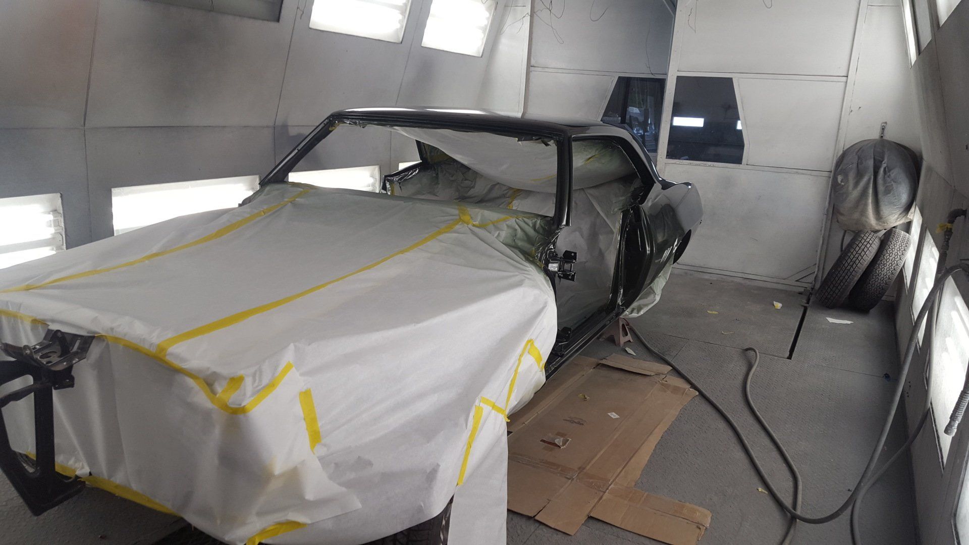 Classic car in a paint booth, covered in protective paper, ready for painting.