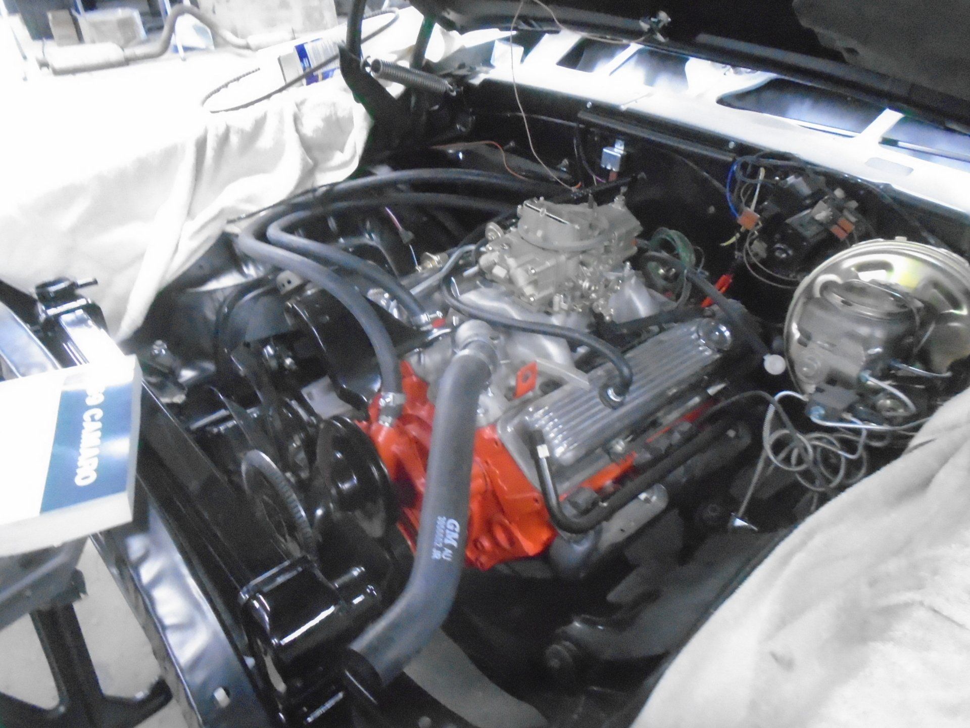 Black classic car engine bay with orange engine, chrome carburetor, and black accessories.
