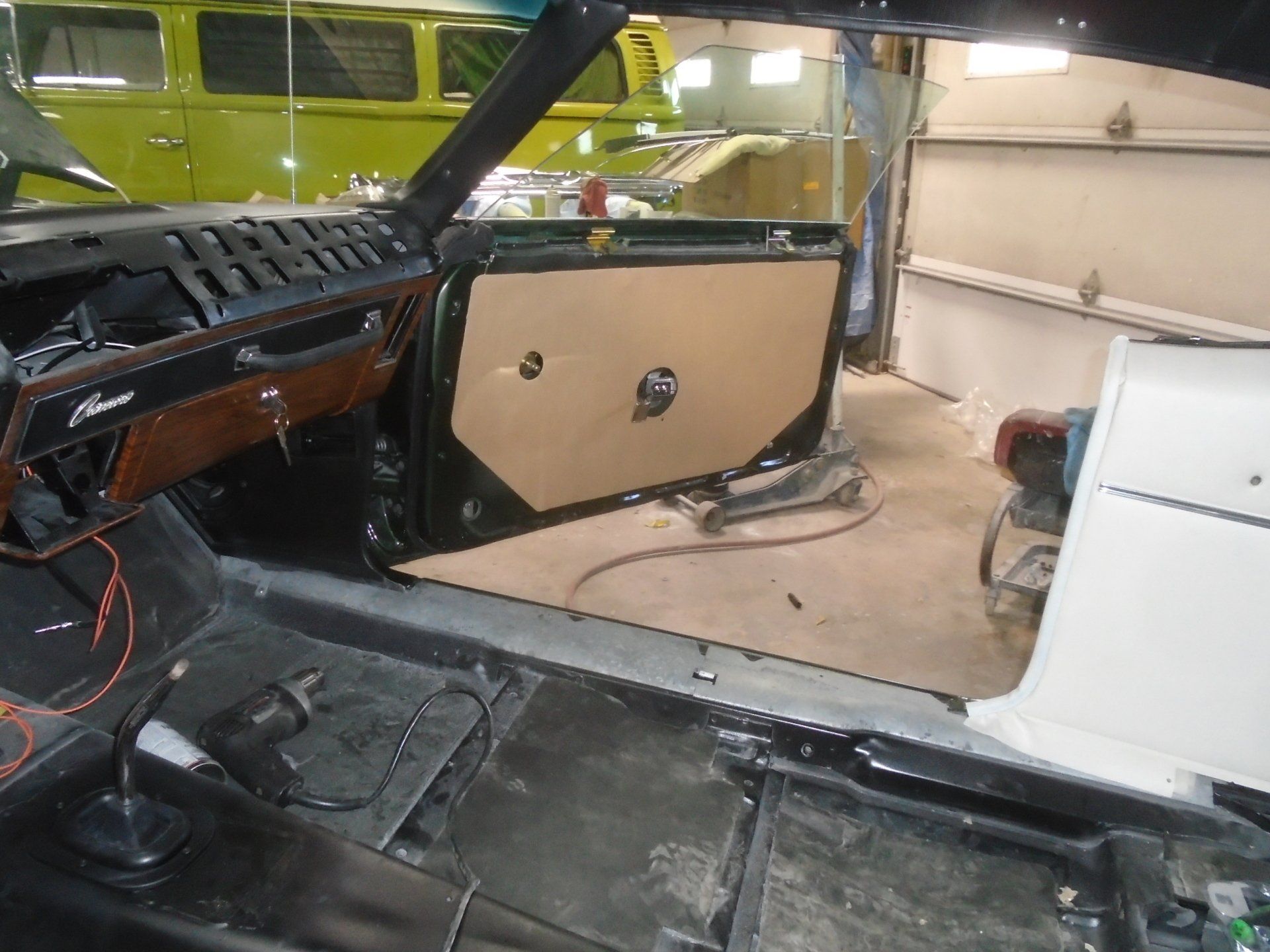 Interior of a classic car under restoration; door panel installed, floor exposed, tools visible in a garage.