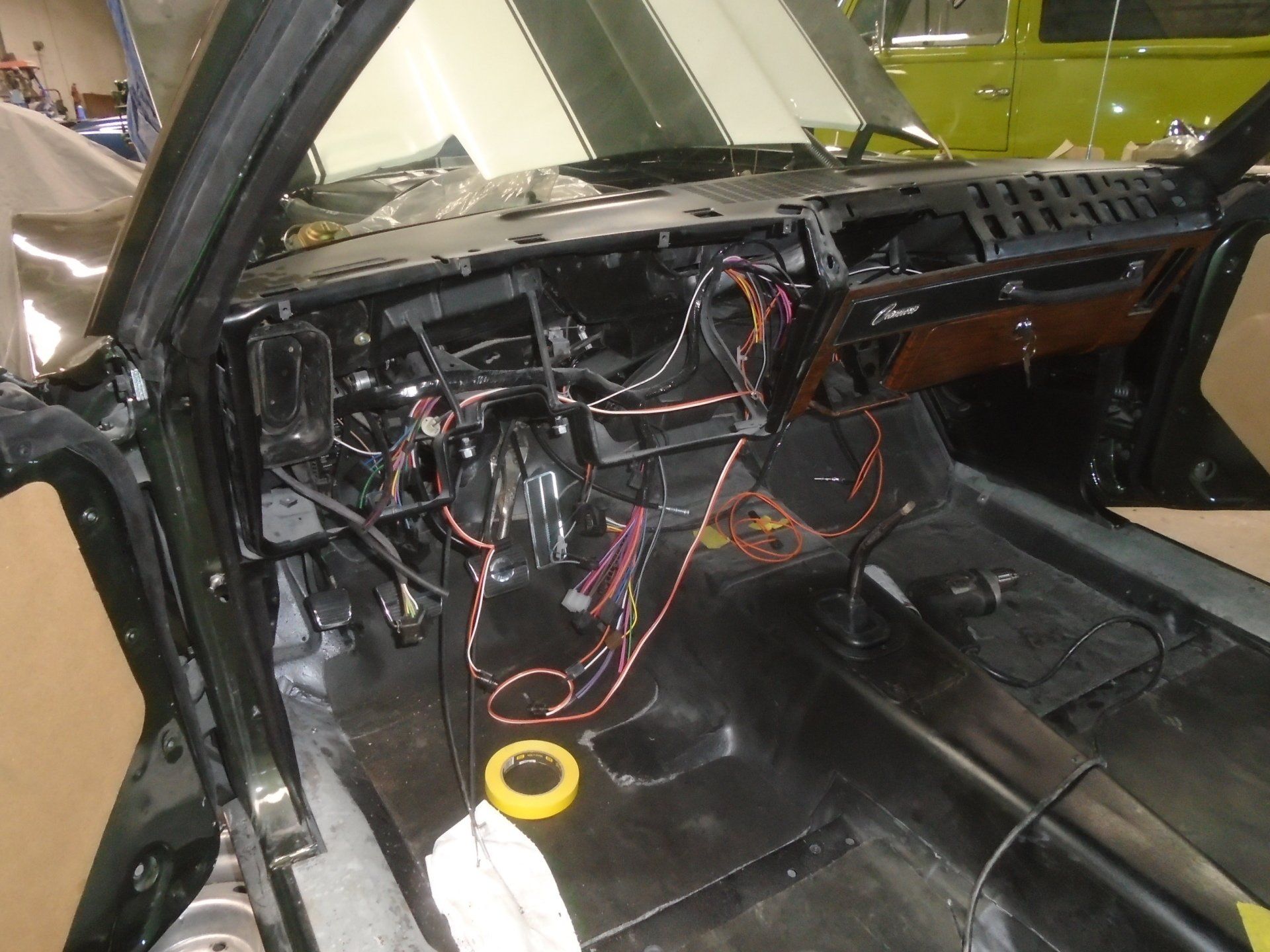 Interior of a classic car under restoration, with exposed wiring and dashboard. Green paint, black interior, and open doors.