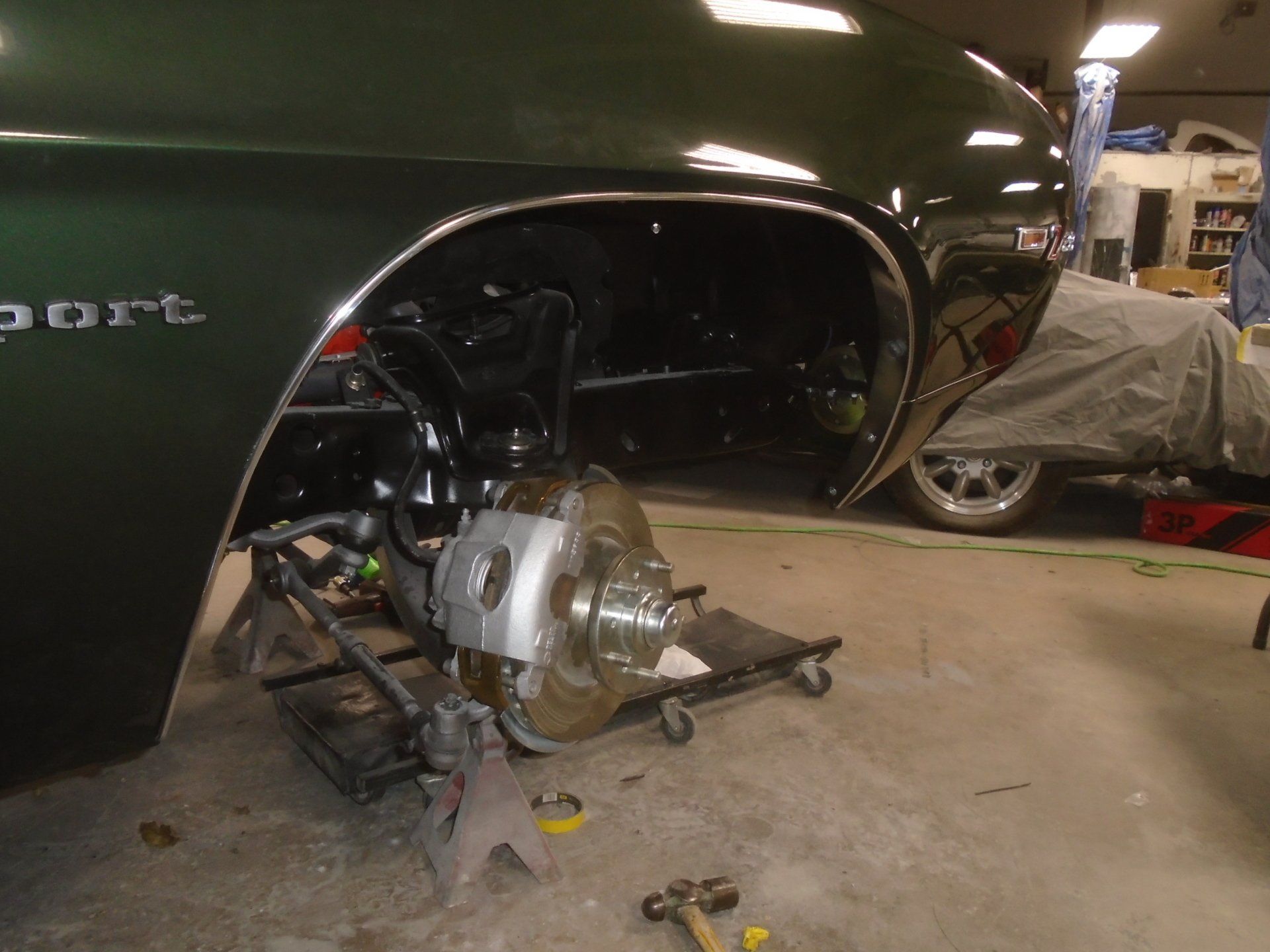 Green classic car front suspension being worked on in a garage.