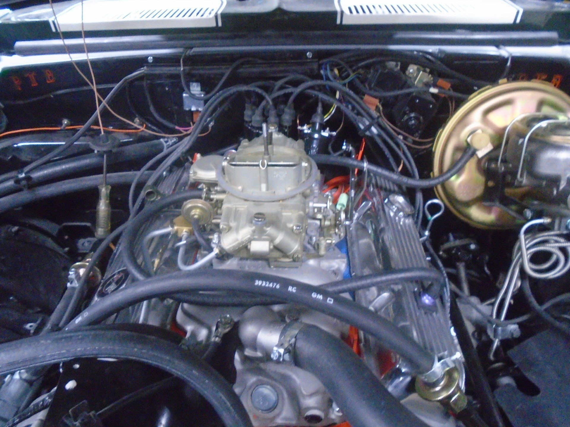 Engine bay of a classic car with a carburetor, chrome details, and various hoses and wires.