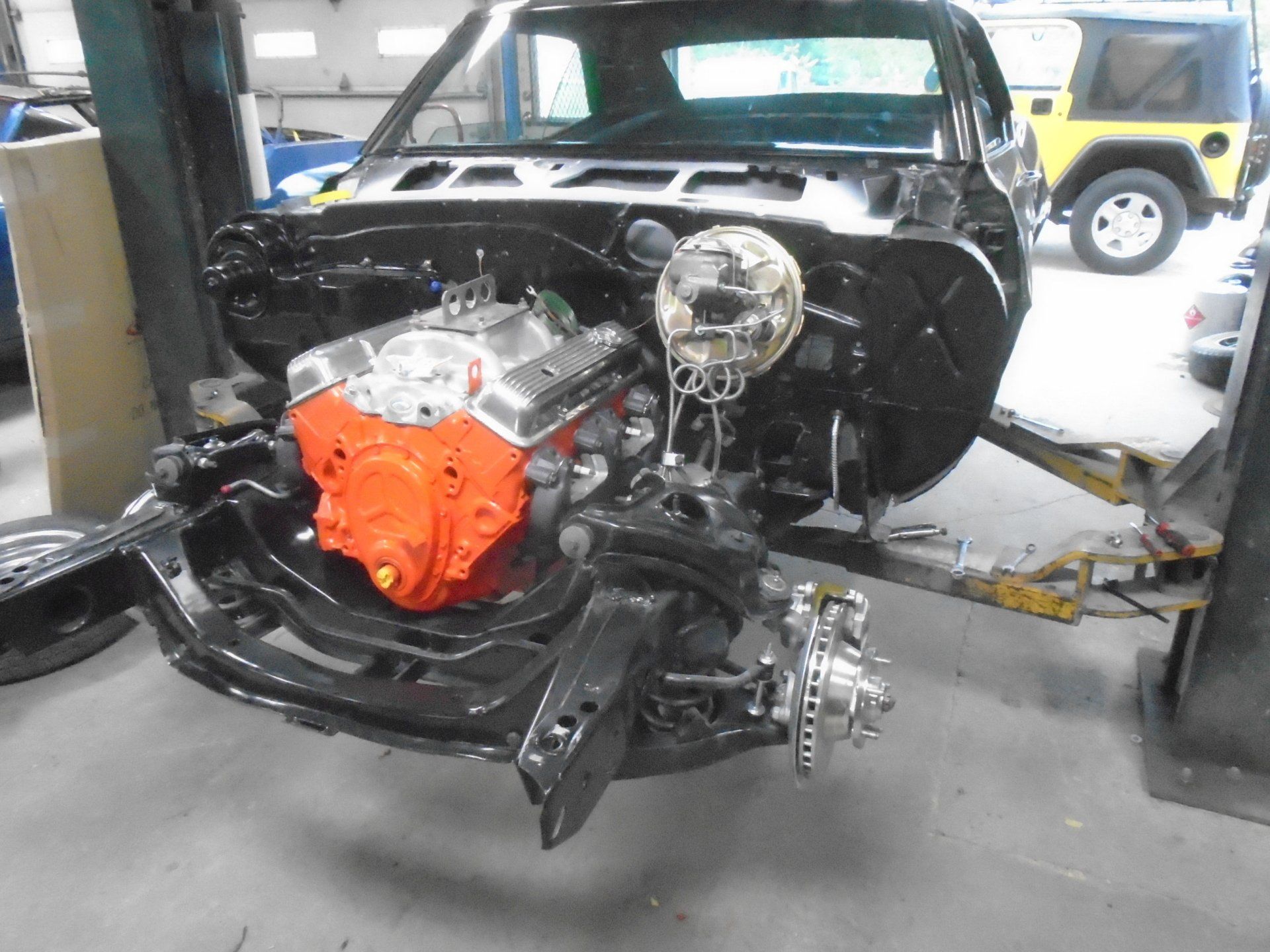 Black classic car frame with an orange engine, under restoration in a garage.