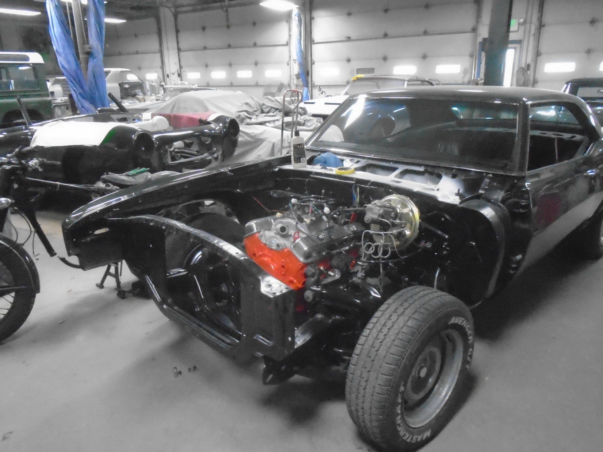 Black classic car undergoing restoration in a shop; engine visible.