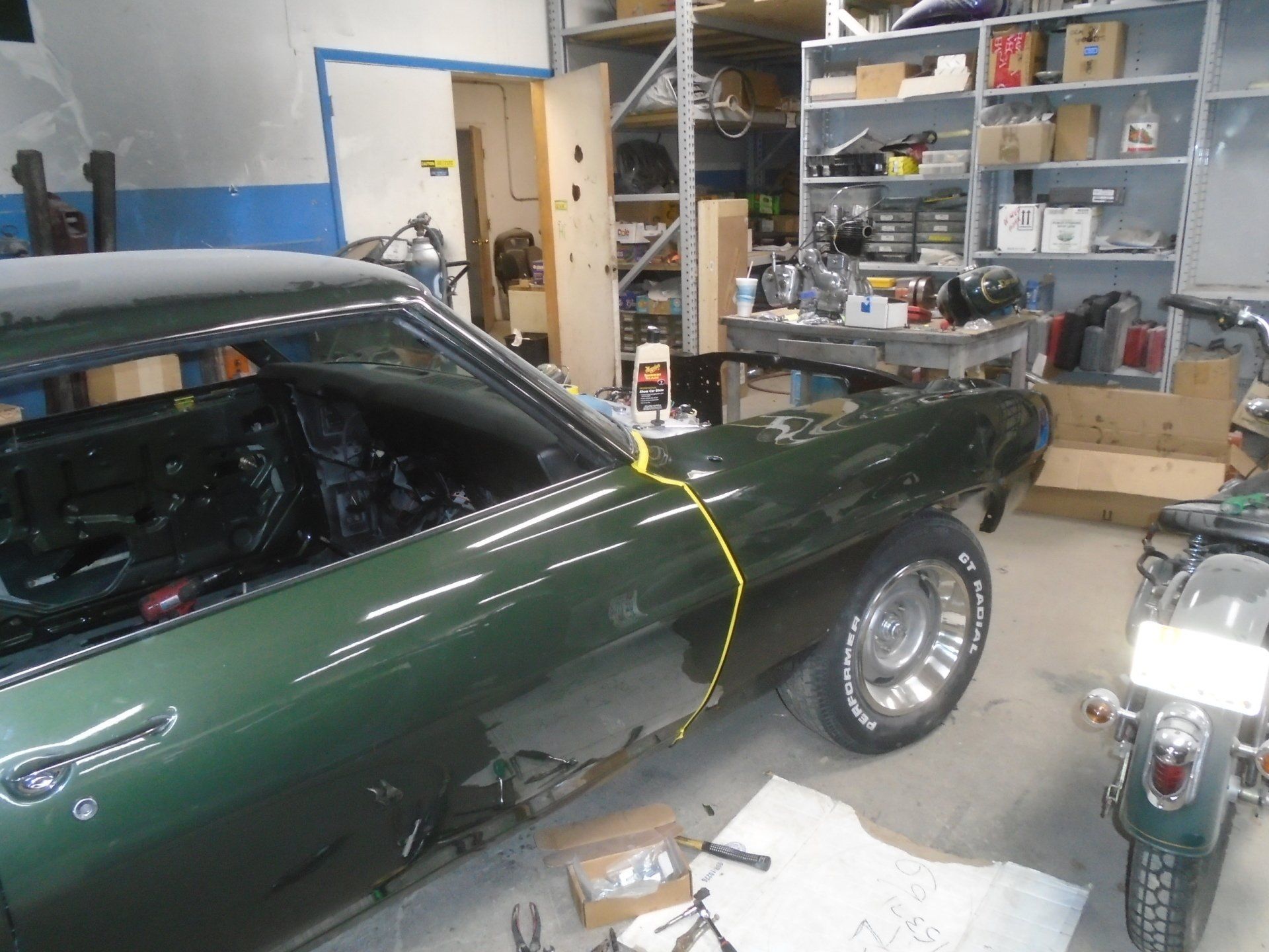 Green classic car in a garage with work in progress, tools, and a motorcycle.