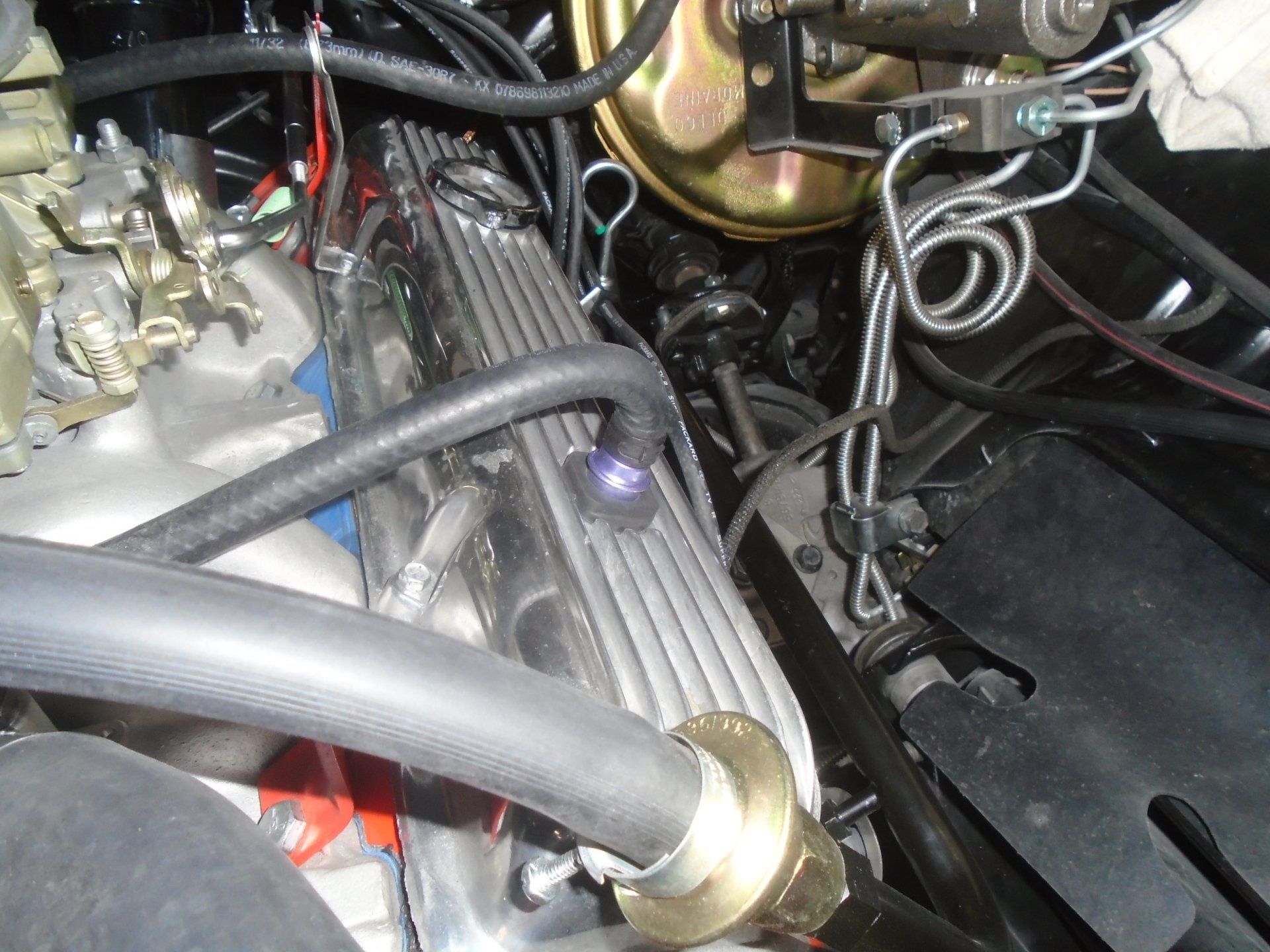 Engine compartment with chrome valve cover, brake lines, and vacuum hose.