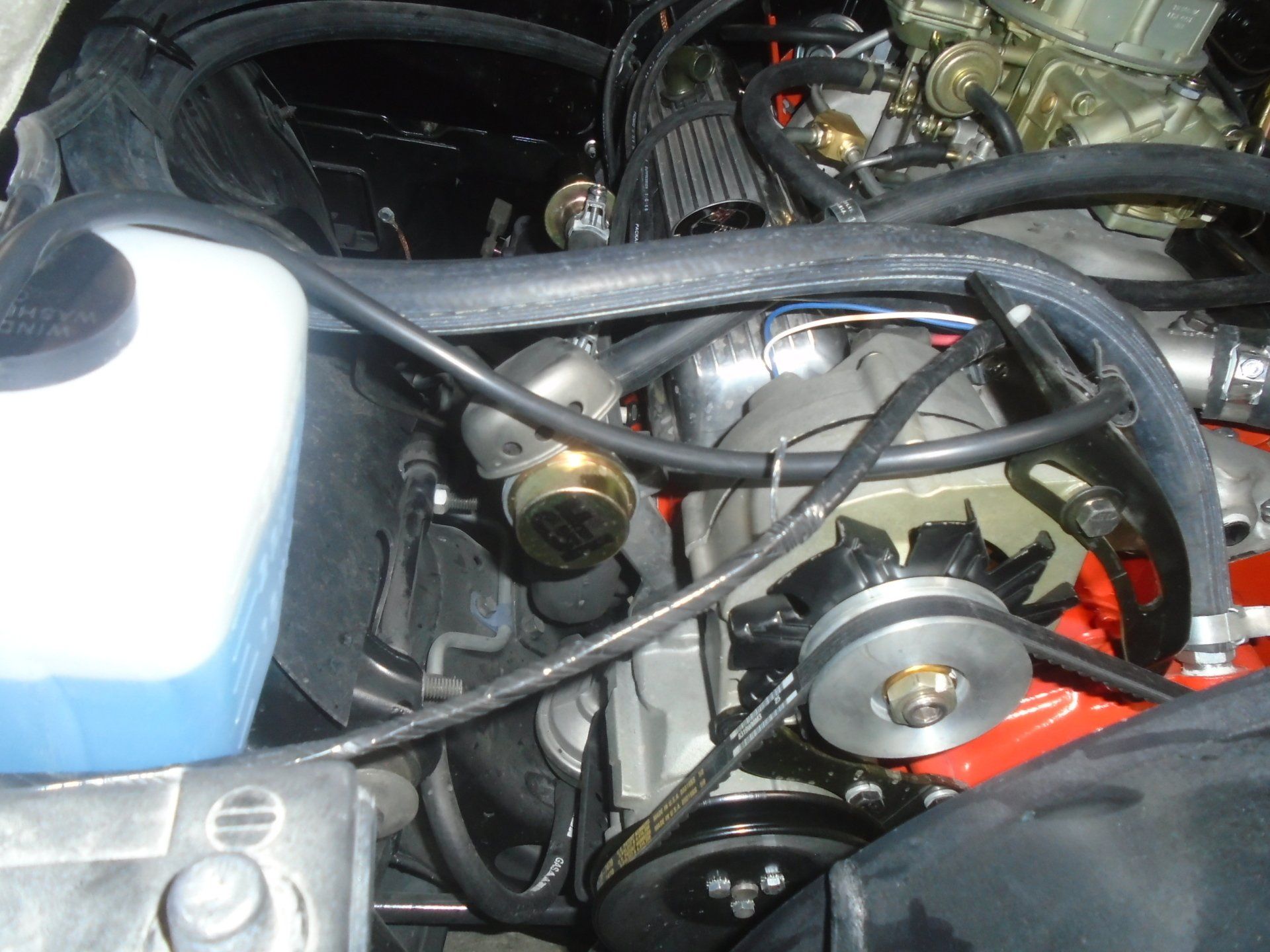 Engine compartment with red engine block, black hoses, water reservoir, and alternator.