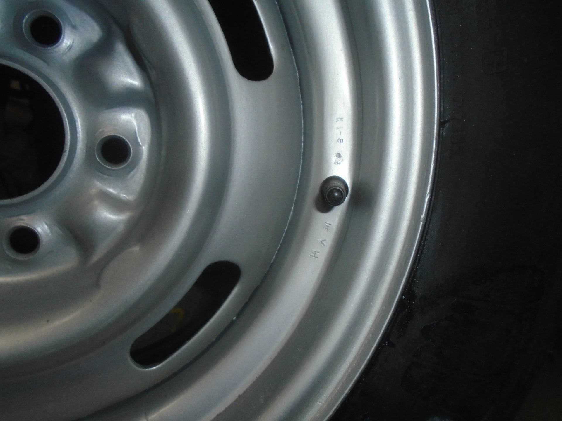 Silver steel wheel with oblong slots and black tire.