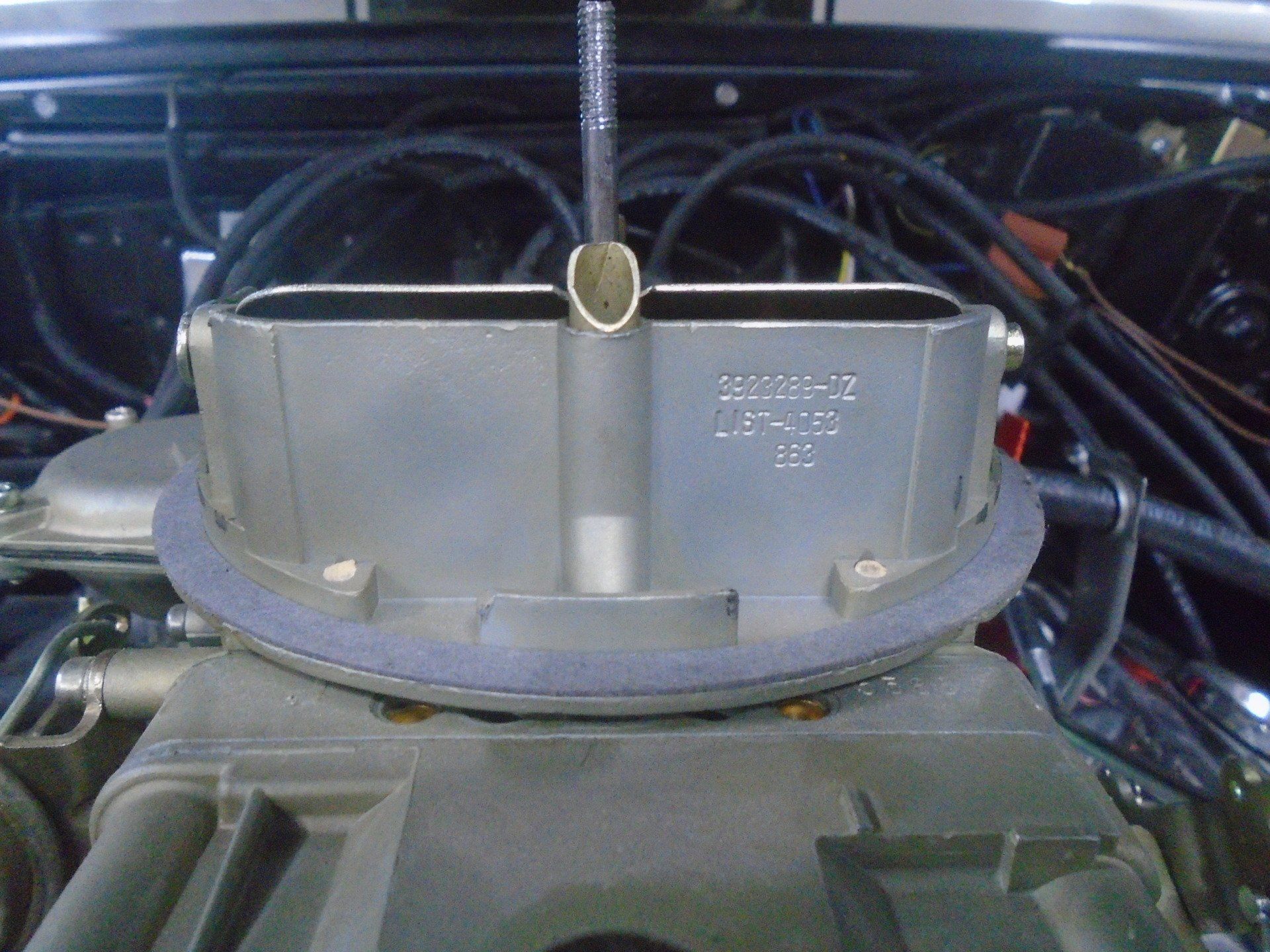 Close-up of a silver carburetor on an engine, with a black air cleaner and wiring in the background.