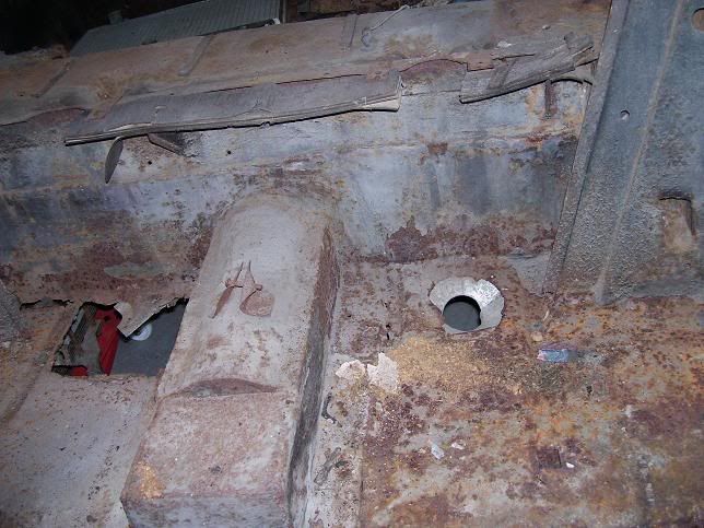 Severely rusted vehicle undercarriage with holes and exposed components.