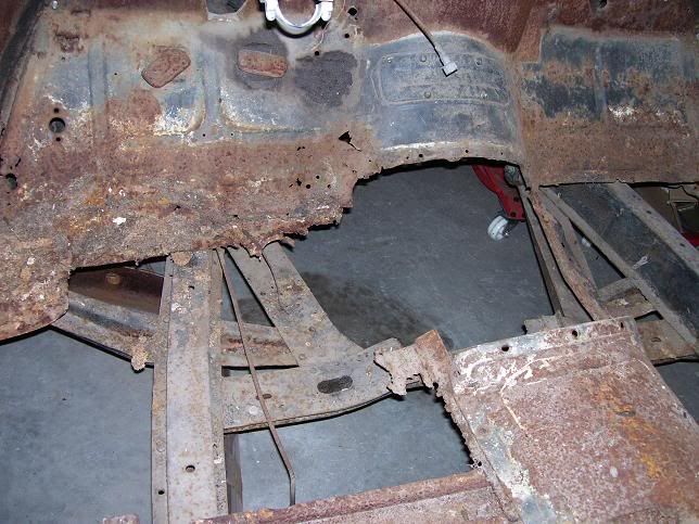 Heavily rusted car floor and frame. Large hole visible in the floor. Rust dominates.