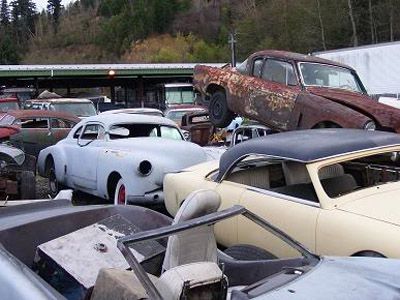 Junk cars piled up in a salvage yard. Rust, weathered paint, and broken parts are visible.