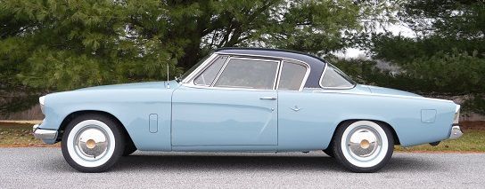 Light blue and black vintage Studebaker car with white tires on a paved road.