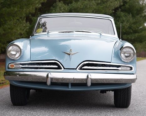 Light blue vintage Studebaker car, front view. Chrome bumper, round headlights, on a paved road.
