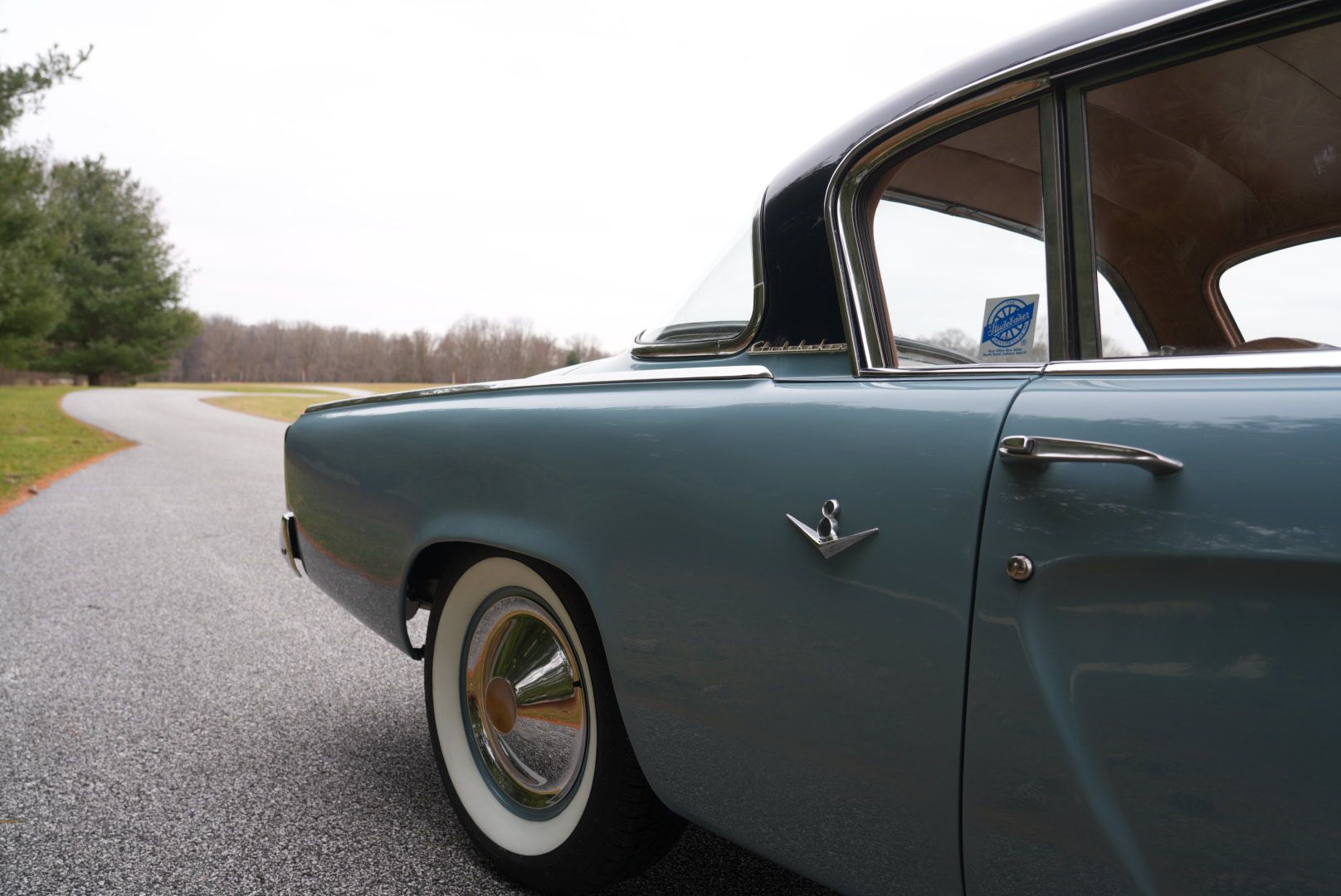 Blue classic car parked on a road, white tires, black roof.