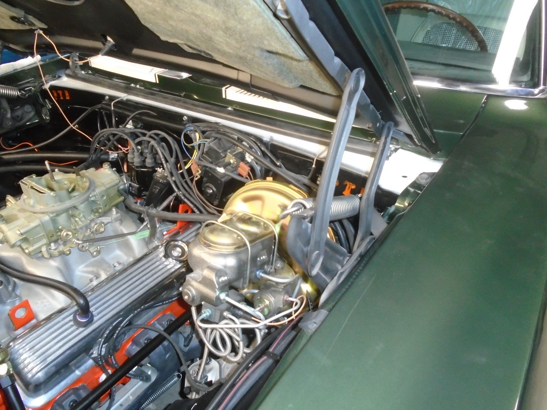 Green classic car engine bay with carburetor, brake components, and wiring.