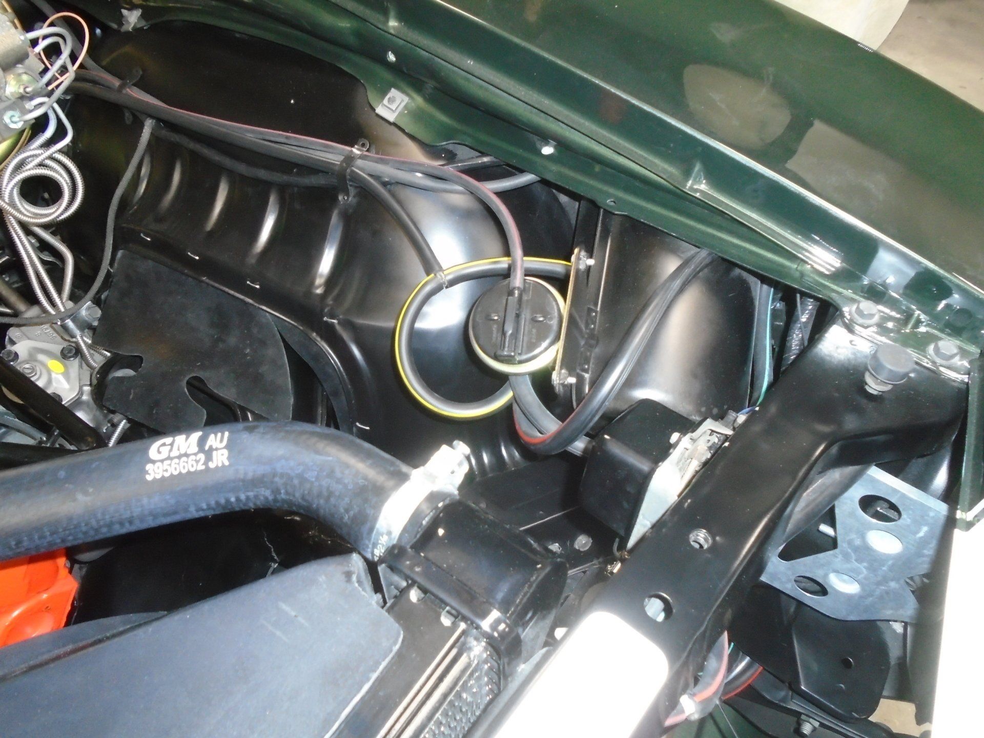 Engine bay of a classic green car; black components, hoses, and wiring.