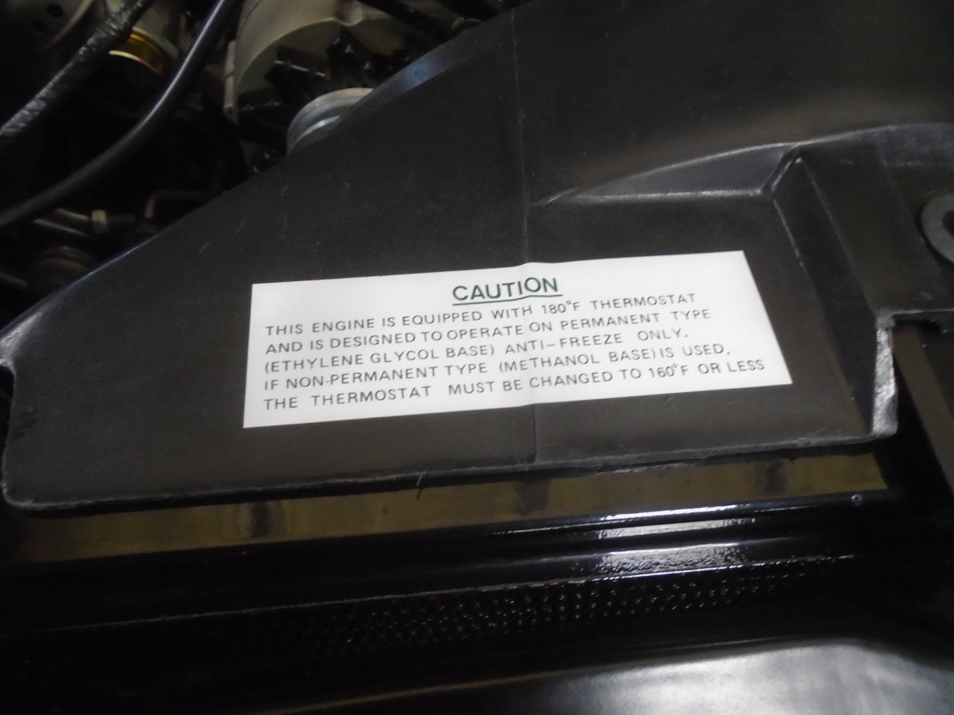 A black engine component with a white sticker stating caution: engine designed for permanent antifreeze 