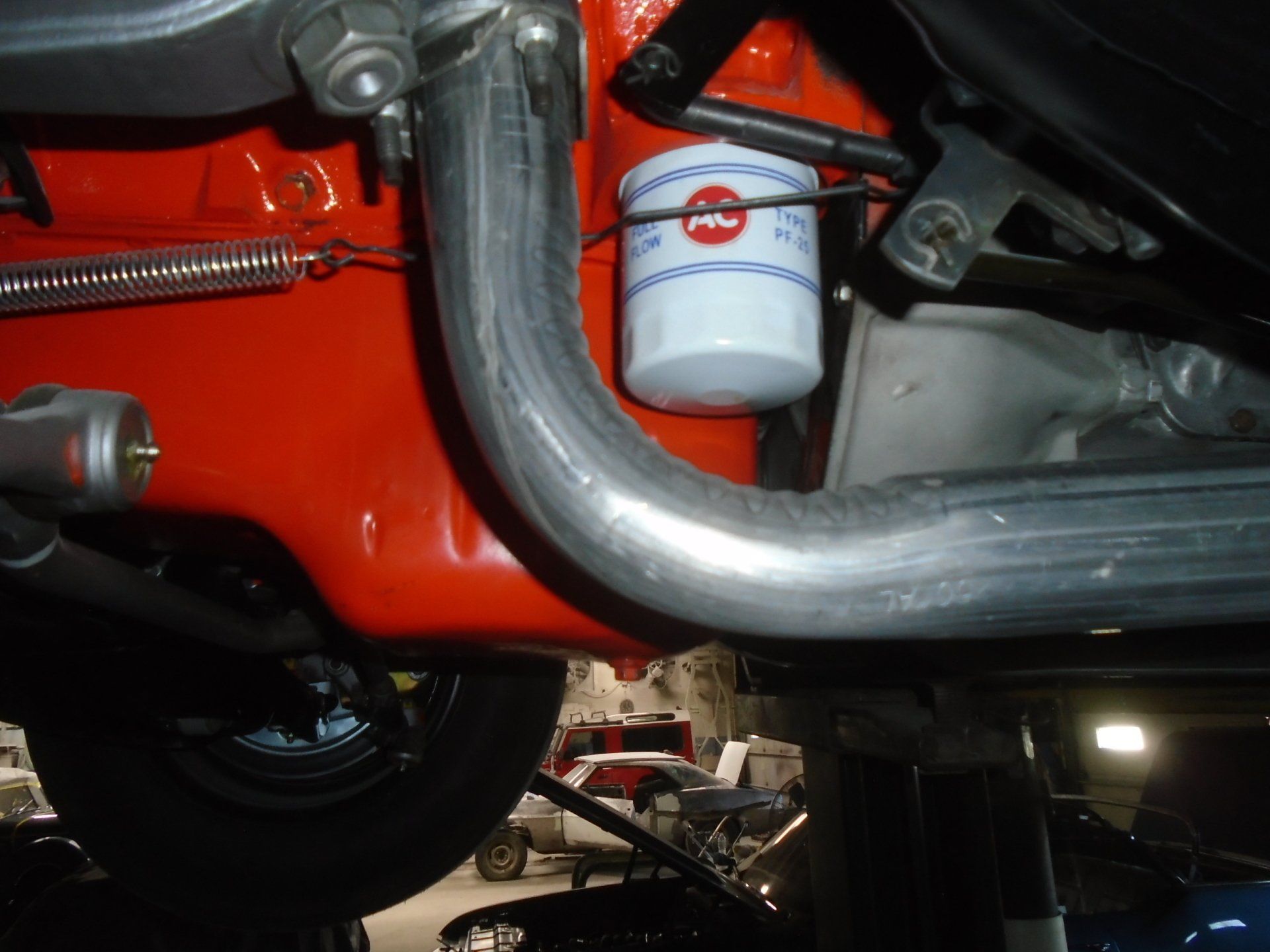 Bright orange engine block with silver exhaust pipe and white oil filter in a garage setting.